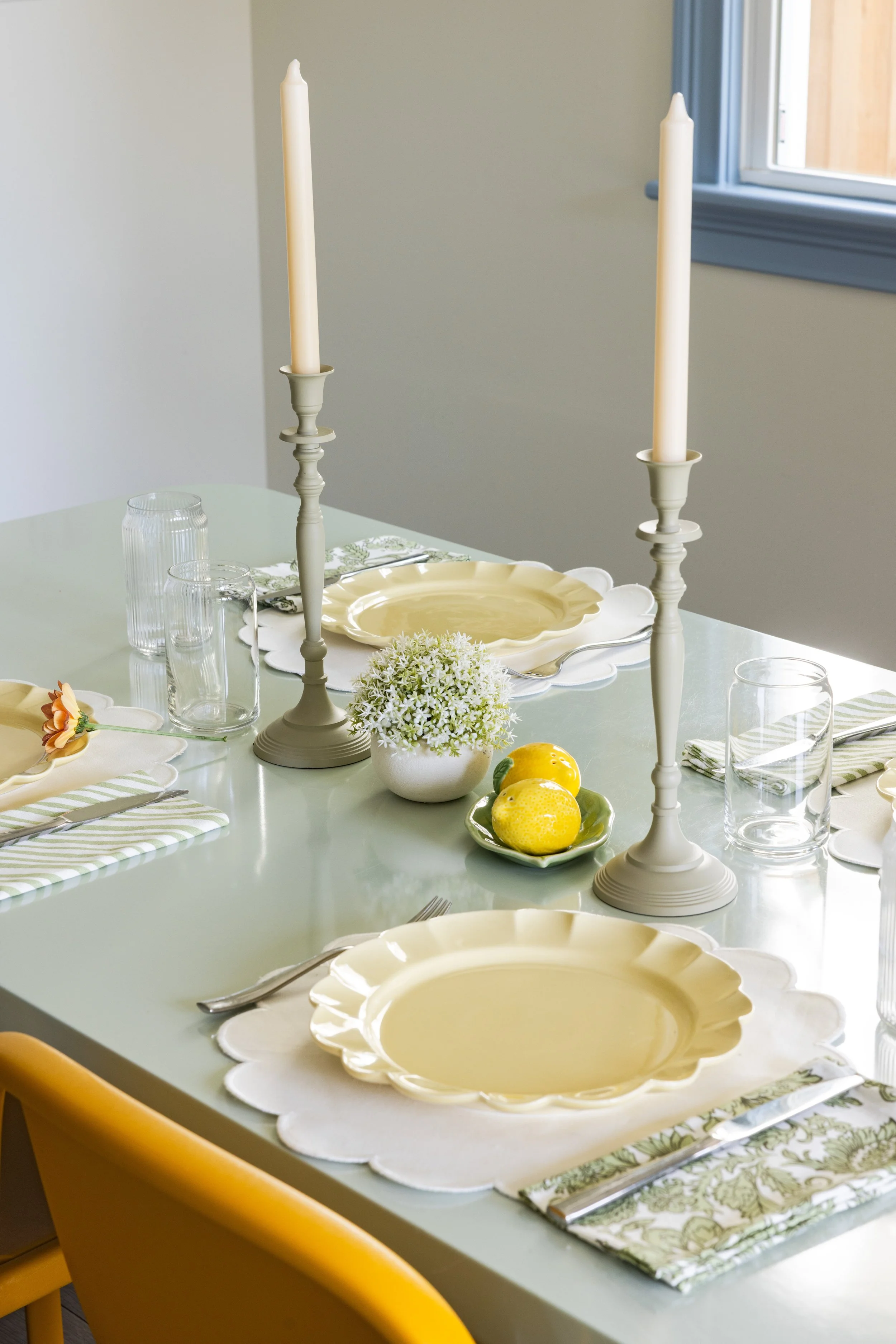 Dining table set with scalloped yellow plates, candlesticks, and lemon accents