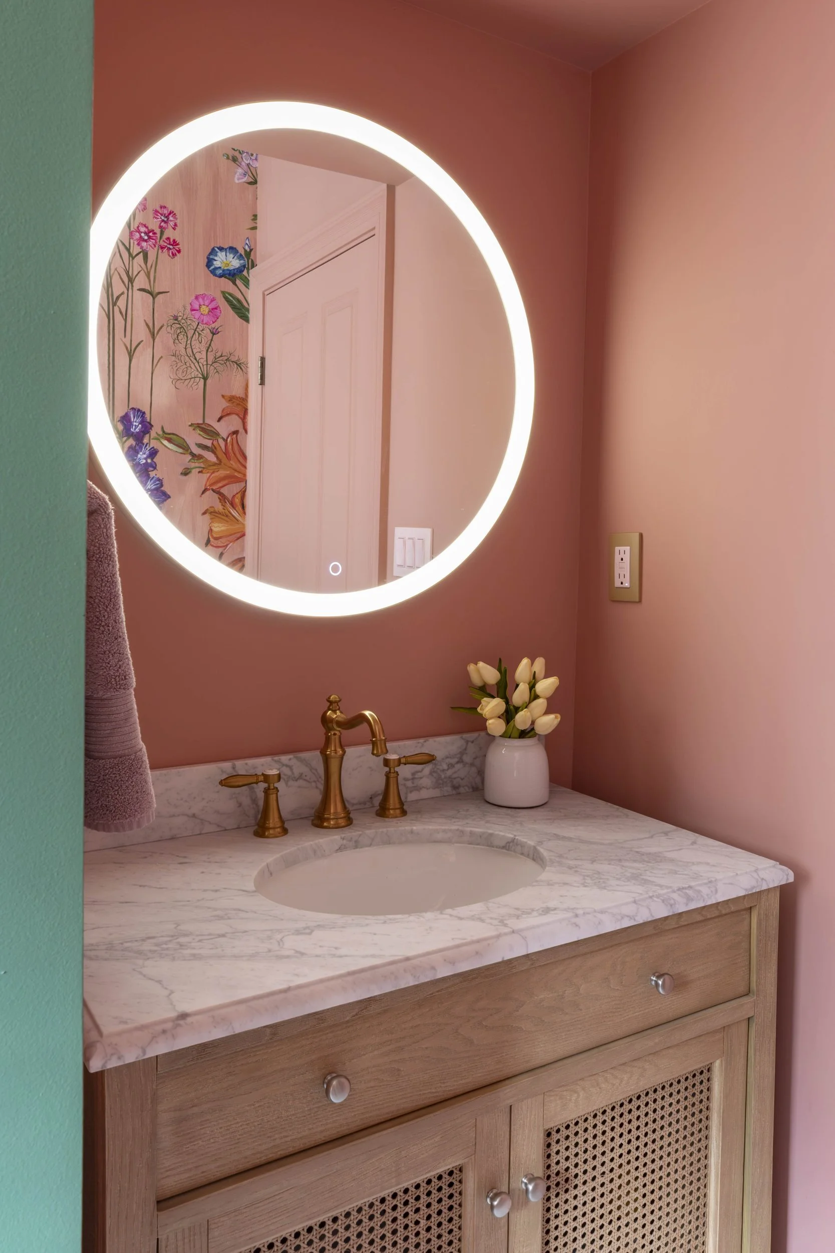 Round lighted mirror over a marble-top vanity with brass faucet