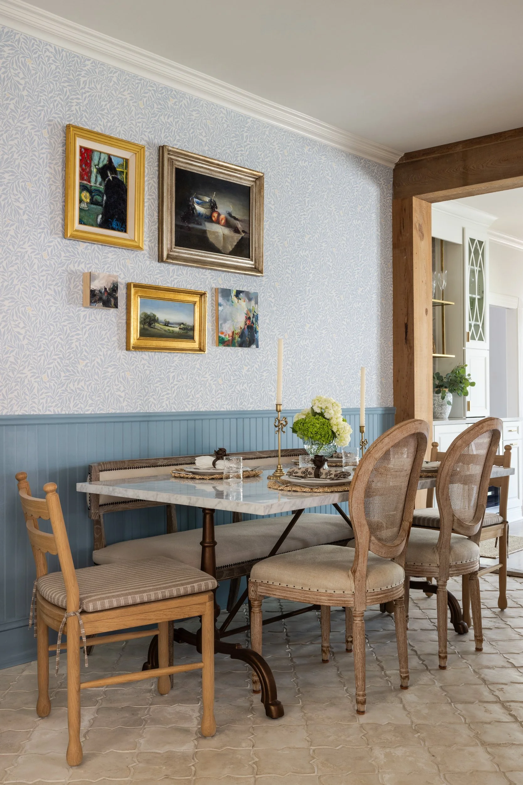 Dining nook with blue leaf wallpaper, blue beadboard, gallery wall, and marble table
