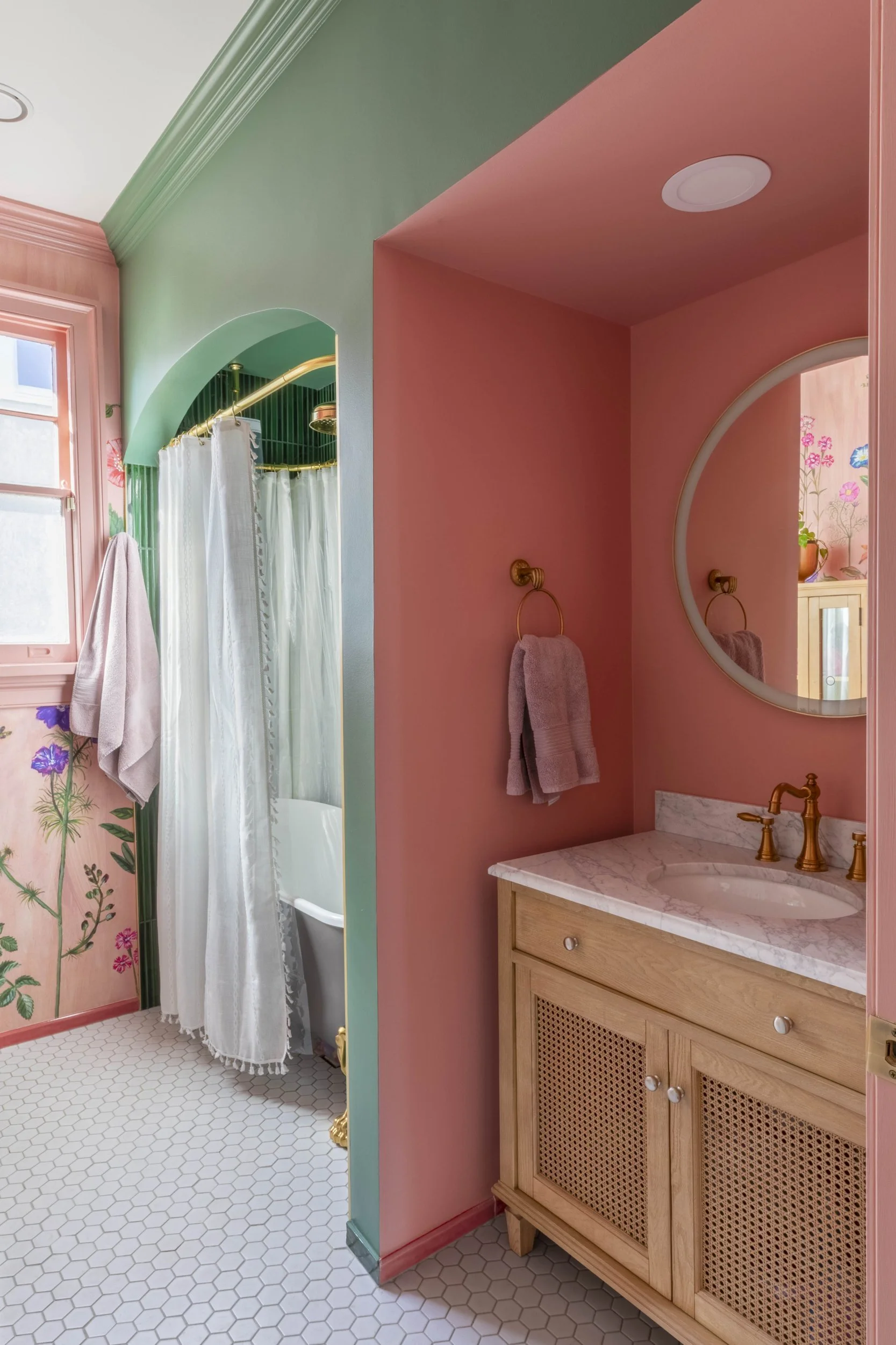 Arched alcove with clawfoot tub beside a pink vanity nook with cane-front cabinet
