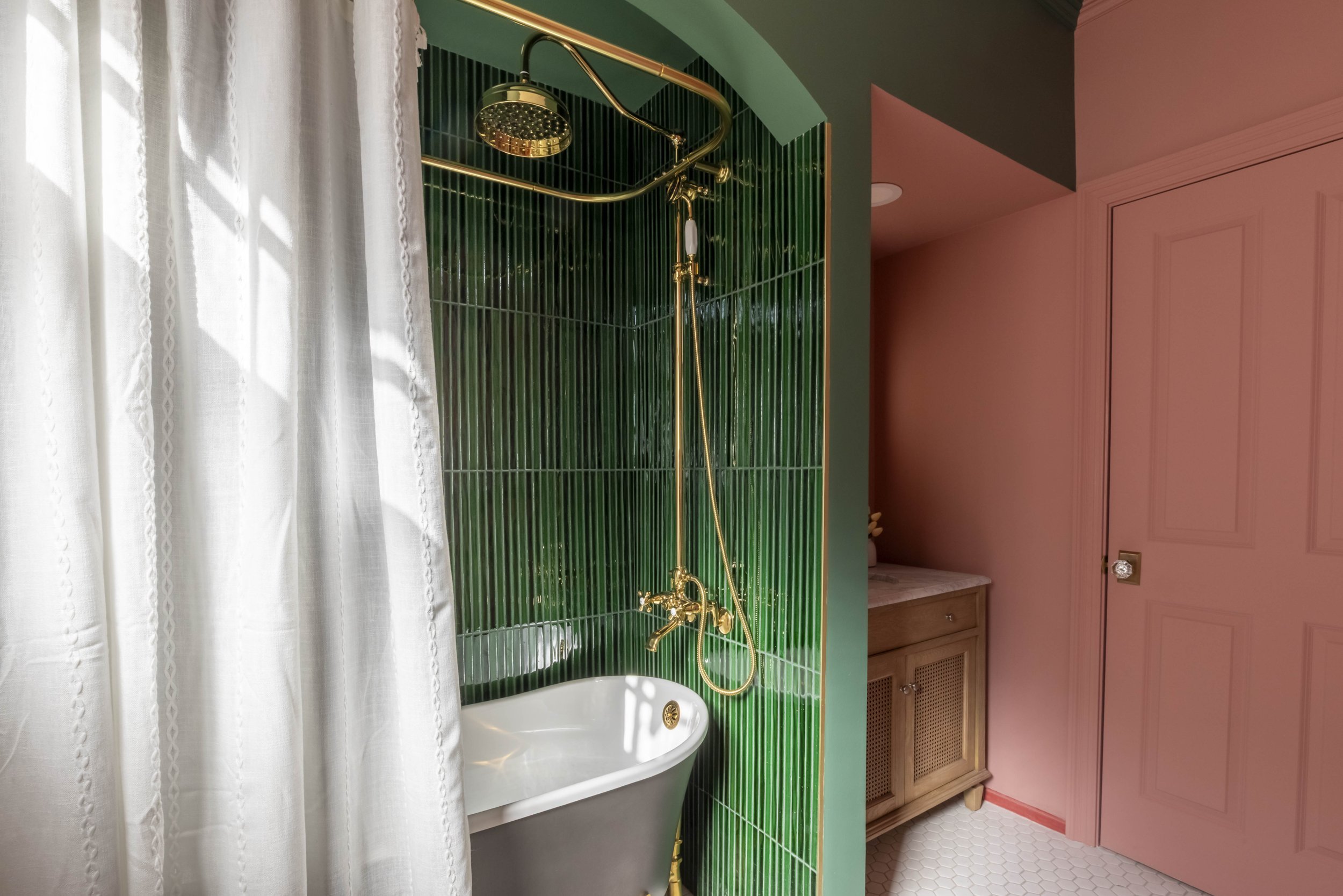 Clawfoot tub against deep green tile with exposed brass shower
