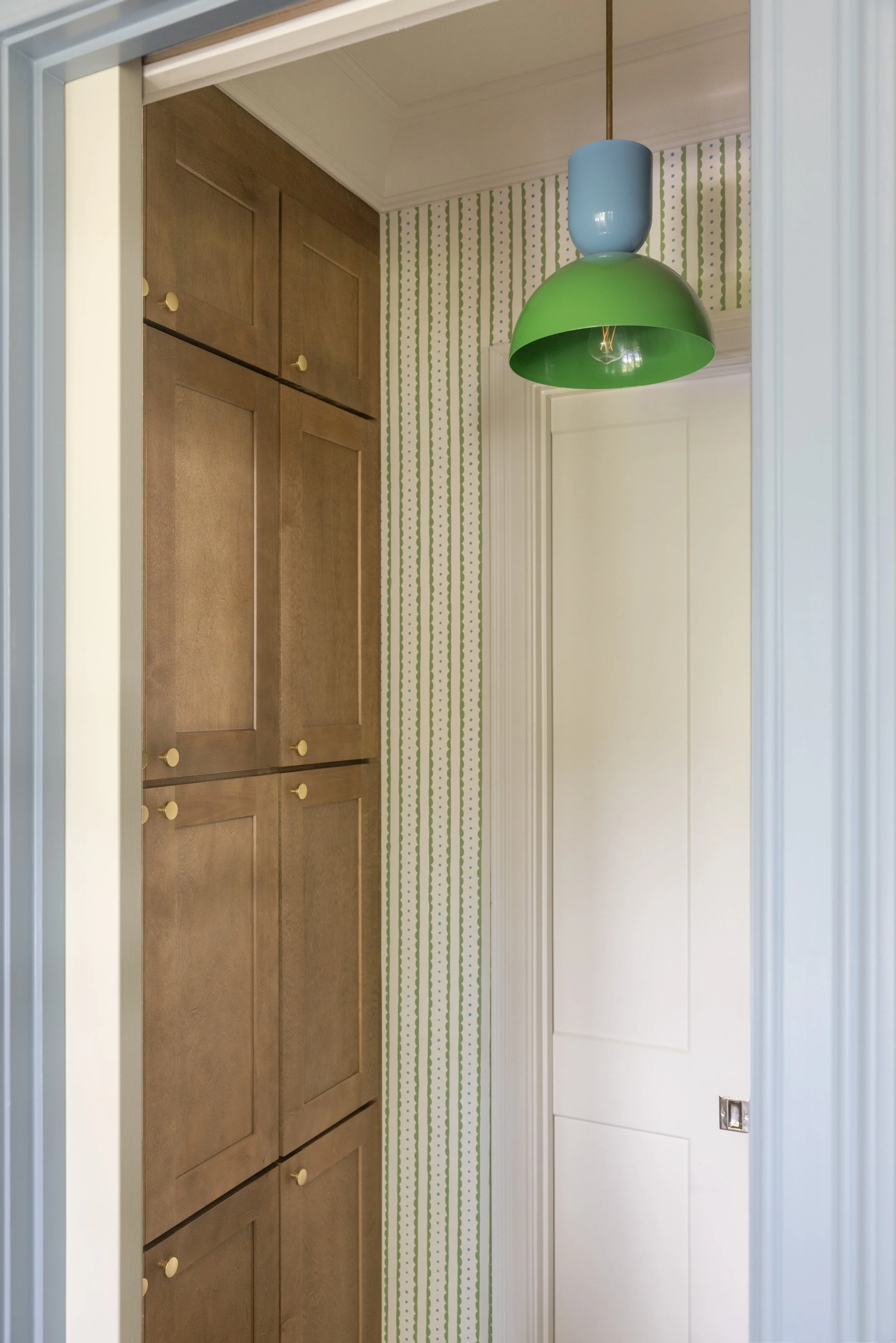 Wood cabinets with green scalloped stripe wallpaper and green pendant light