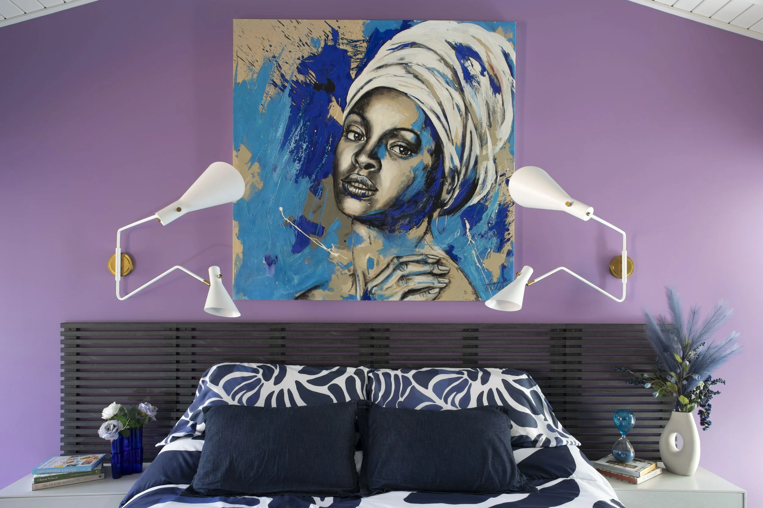 Primary bedroom with lavender wall, blue portrait painting, and double-arm sconces