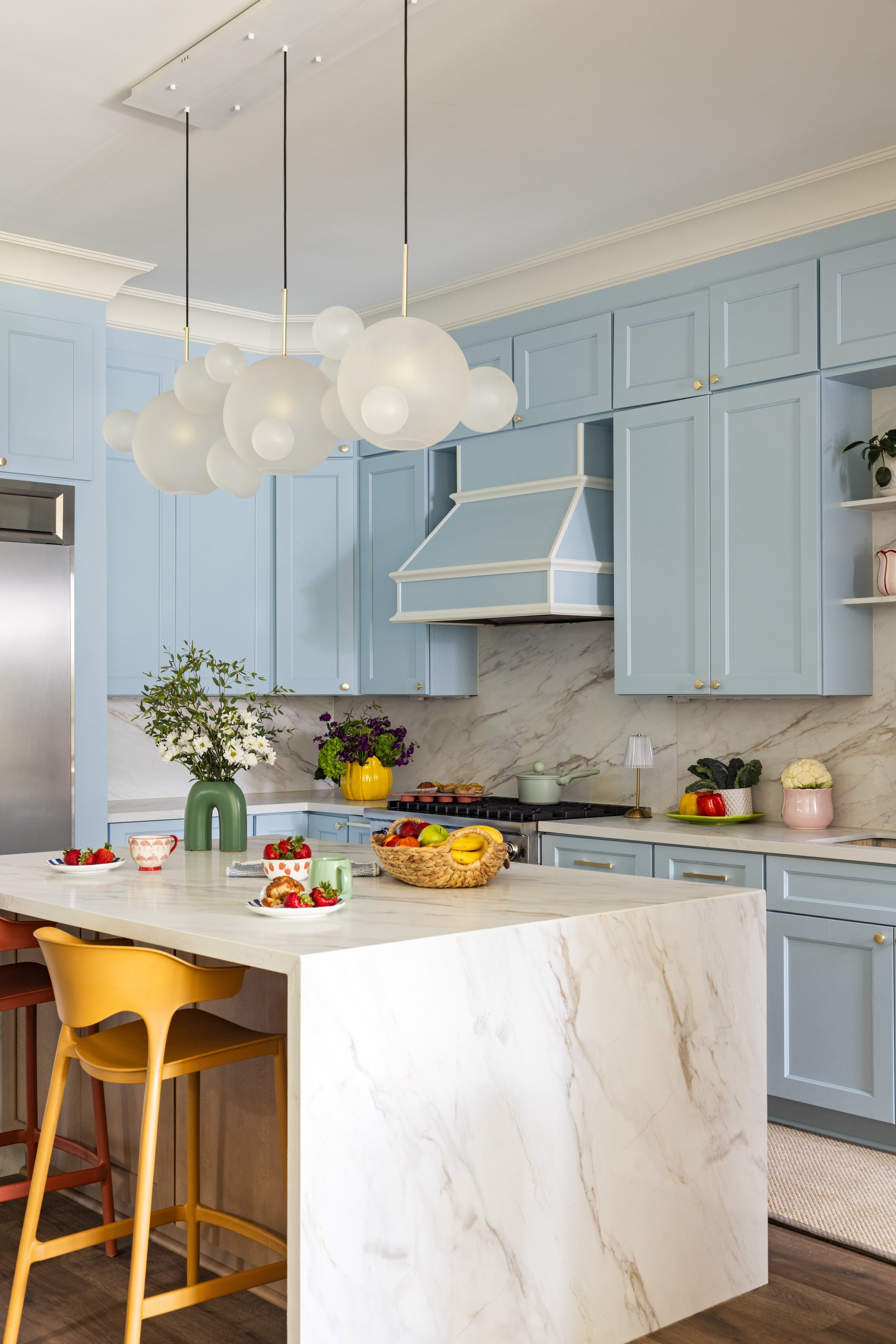 Marble waterfall island with coral and mustard counter stools