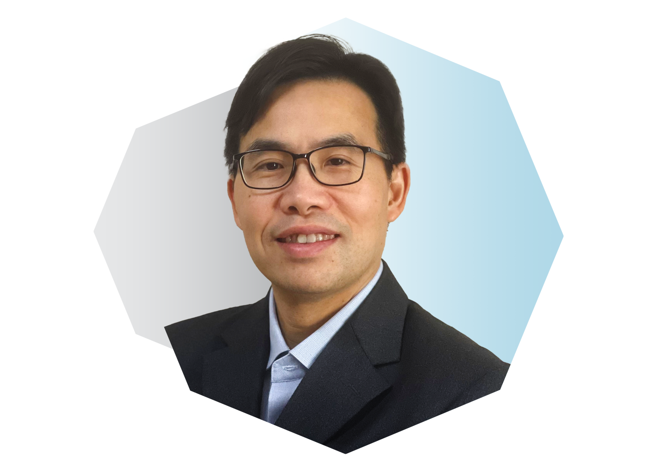 A portrait of a smiling Asian man wearing glasses, a dark blazer, and a light blue shirt.