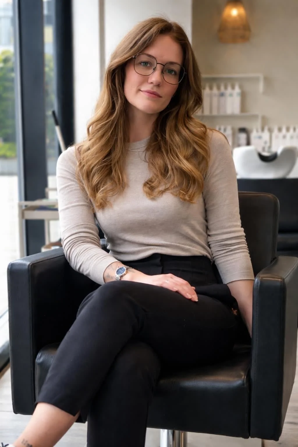 Femme aux cheveux longs et bouclés portant des lunettes, assise dans un salon moderne.