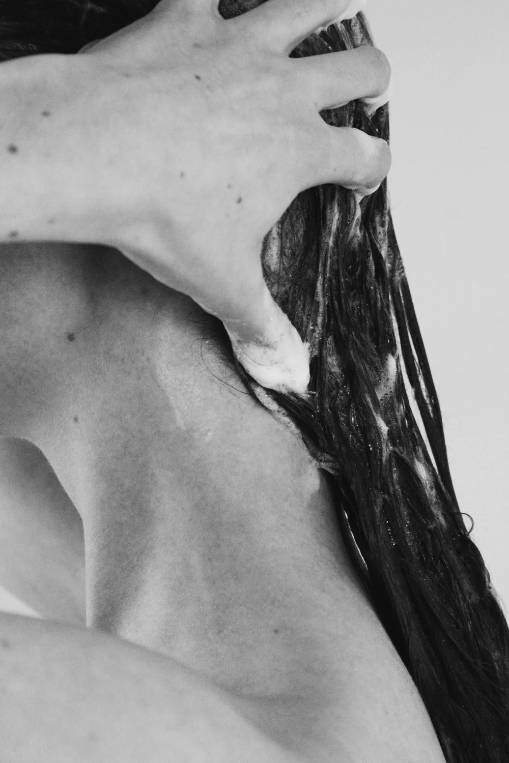 Un gros plan d'une personne lavant ses cheveux longs avec de la mousse, vue de profil, en noir et blanc.