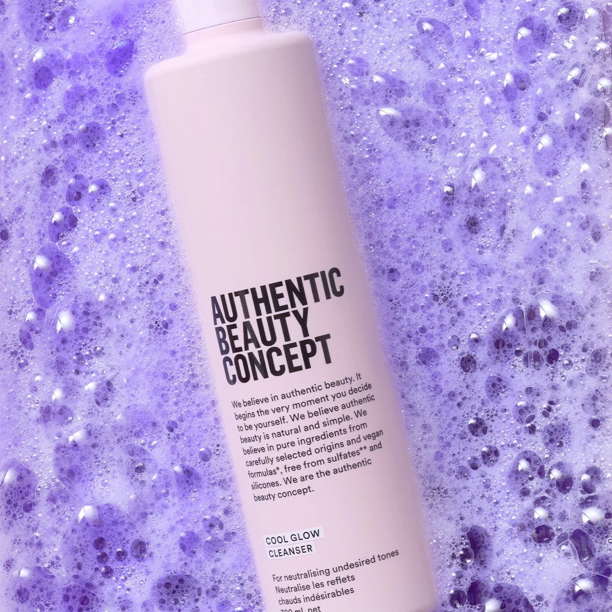 Un flacon blanc d'Authentic Beauty Concept placé dans de la mousse violette, qui semble être un nettoyant visage ou un produit de soin de la peau.