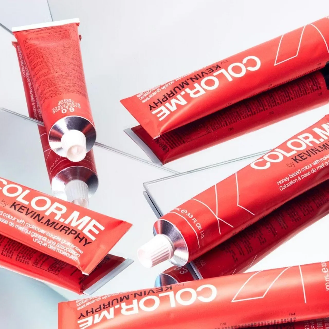 Several red tubes of color cosmetic product with white caps, placed on a reflective surface with a mirror reflecting them.