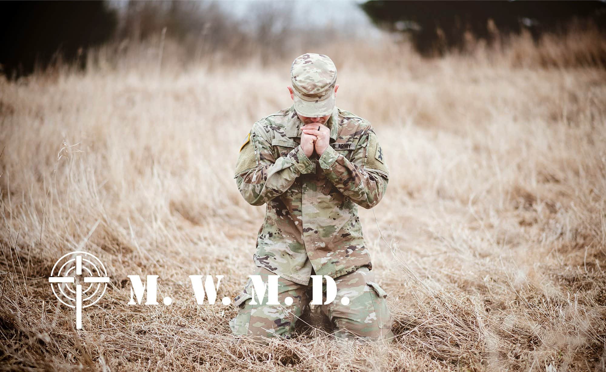A soldier kneeling in dry grass with hands clasped in prayer, wearing camouflage uniform and cap, with the words 'M. W. M. D.' and a crosshair symbol overlayed.