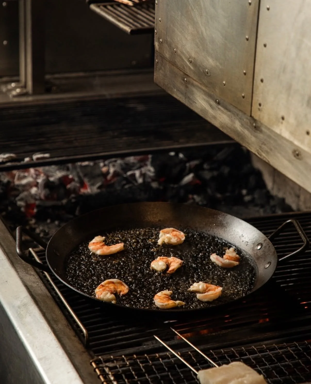 Black rice paella in the making at @34neworleans 🔥

Fun Fact: Our ETL approved wide smoke box, was designed and sized specifically to contain paella pans on request from the Emeril Team. And that is how every new product comes begins.
We build with 