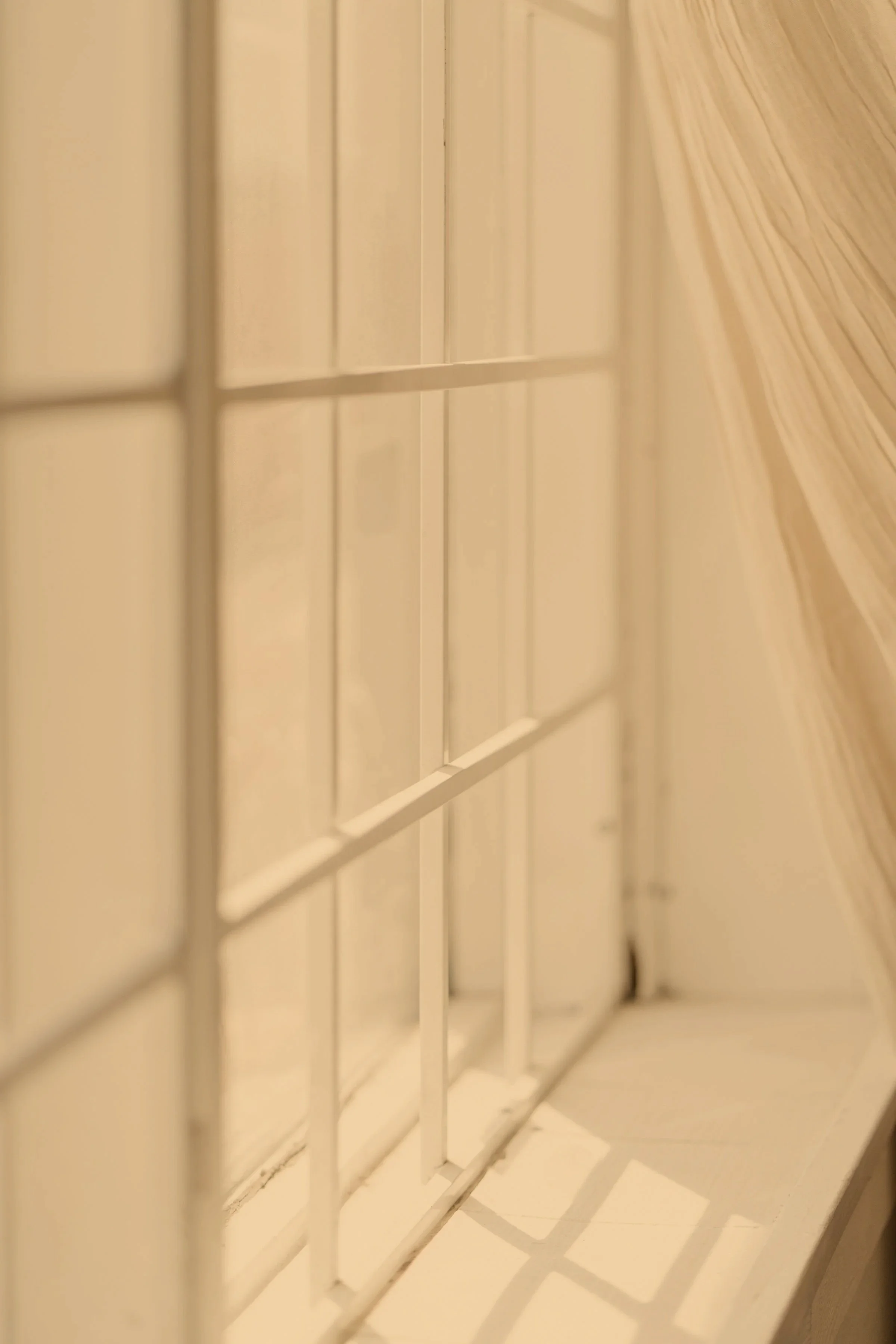Close-up of white window blinds with light filtering through, creating shadows on a wooden surface.