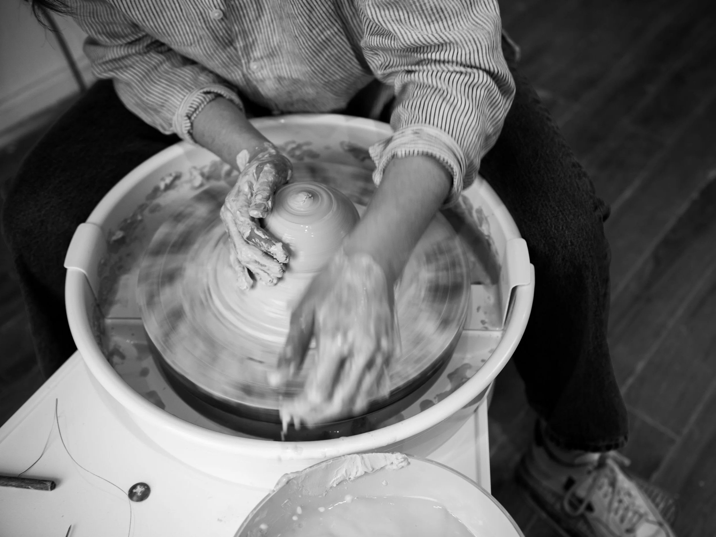 Person shaping clay on a spinning pottery wheel with hands covered in clay.