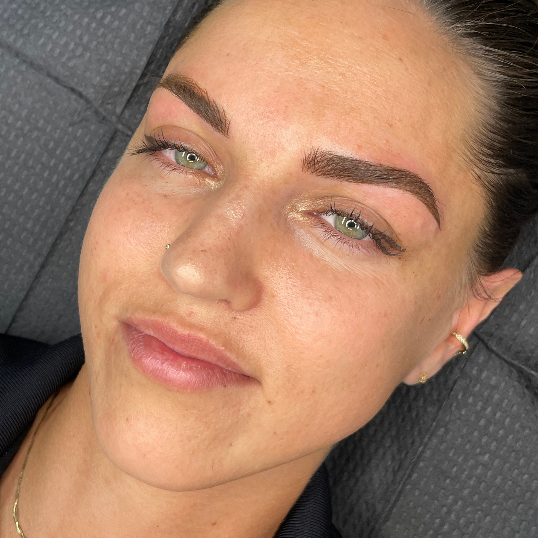 Close-up of a person with green eyes and dark eyebrows, against a textured background.
