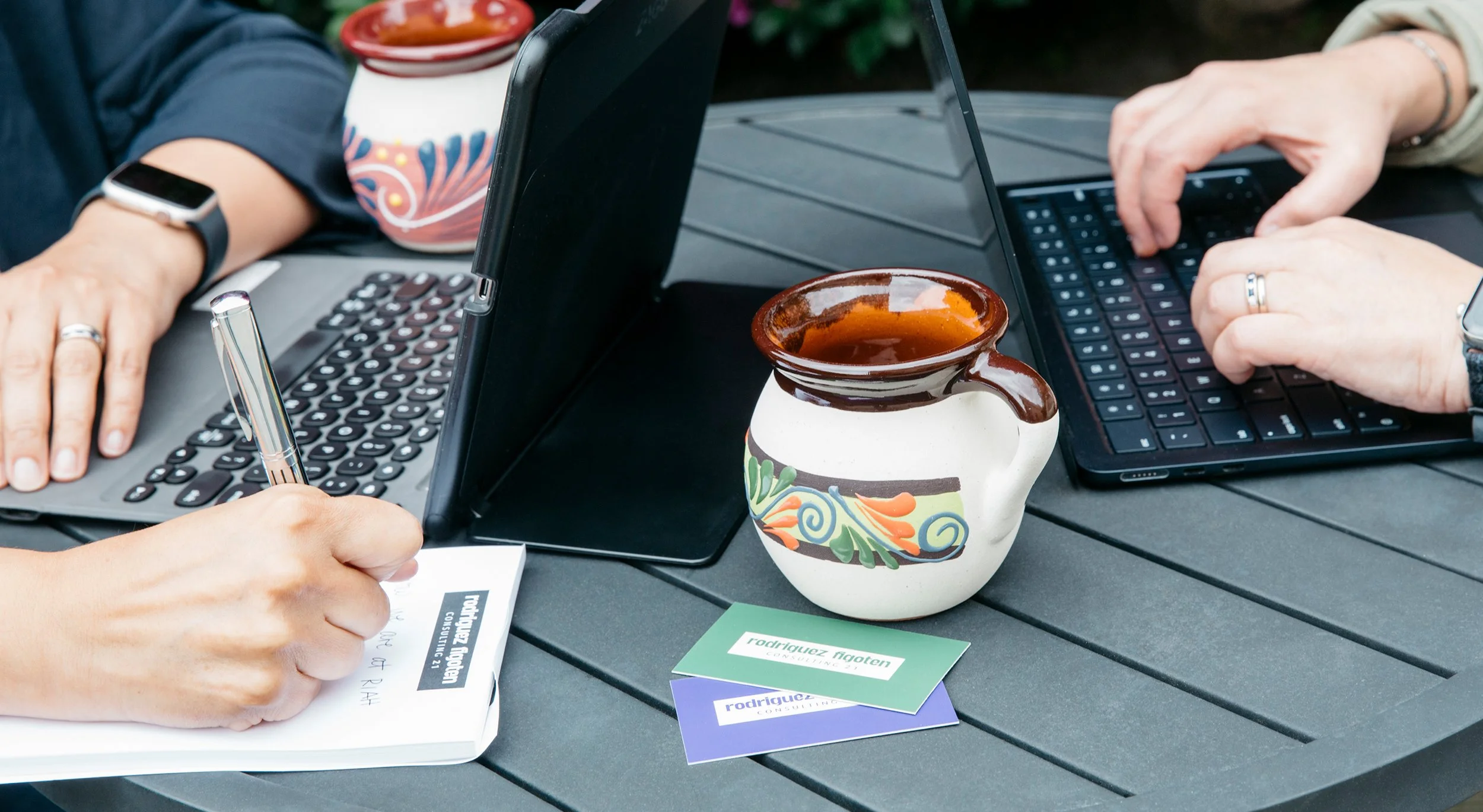 Two women on laptops and writing with a talavera Mexican mug at the center