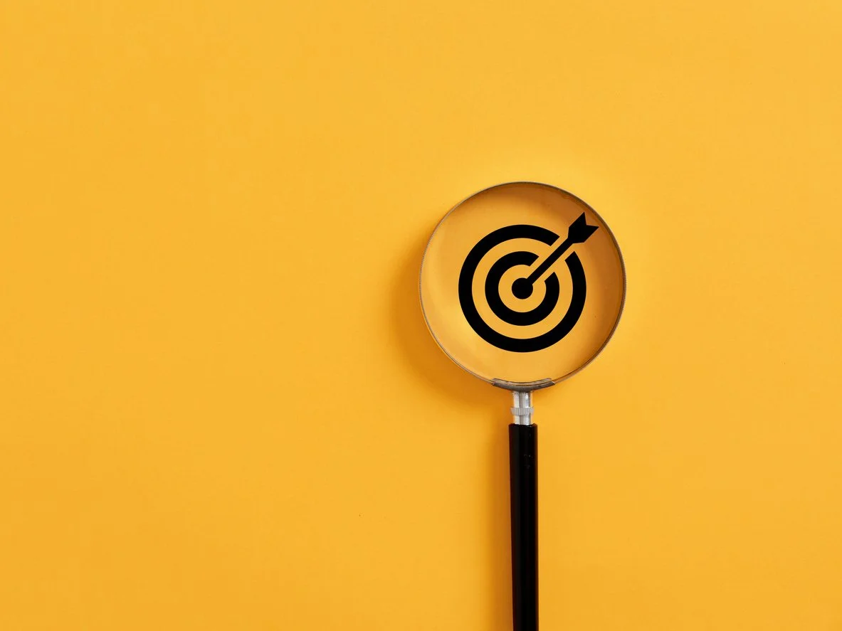 a magnifying glass showing an arrow in the middle of a black circle target
