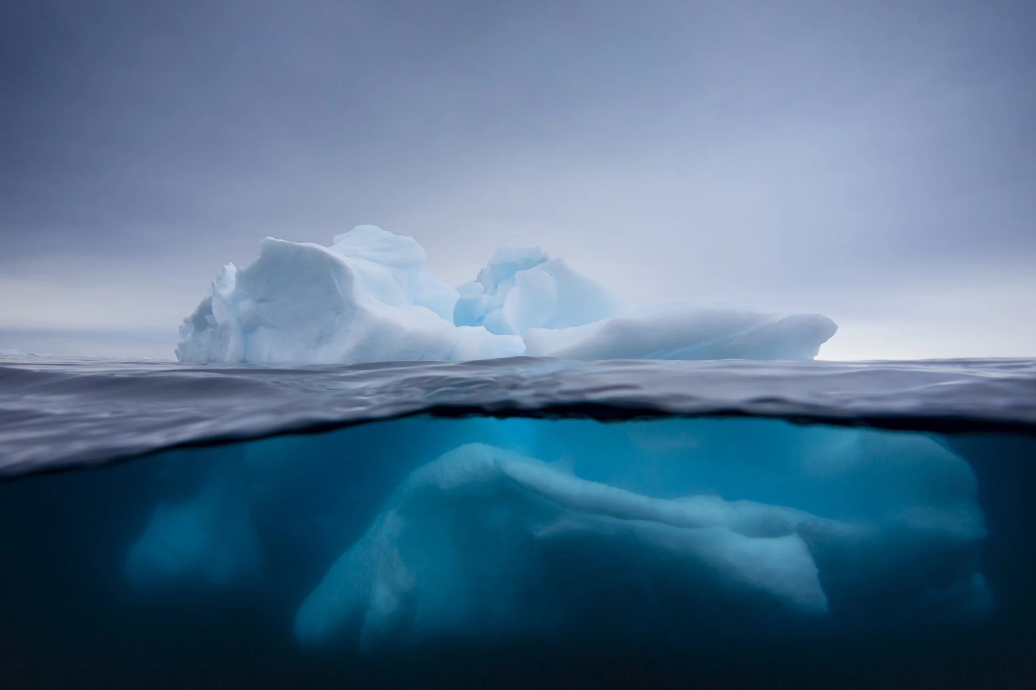 Iceberg photographed half above and half below the waterline, showing the small visible tip and the large hidden mass beneath.