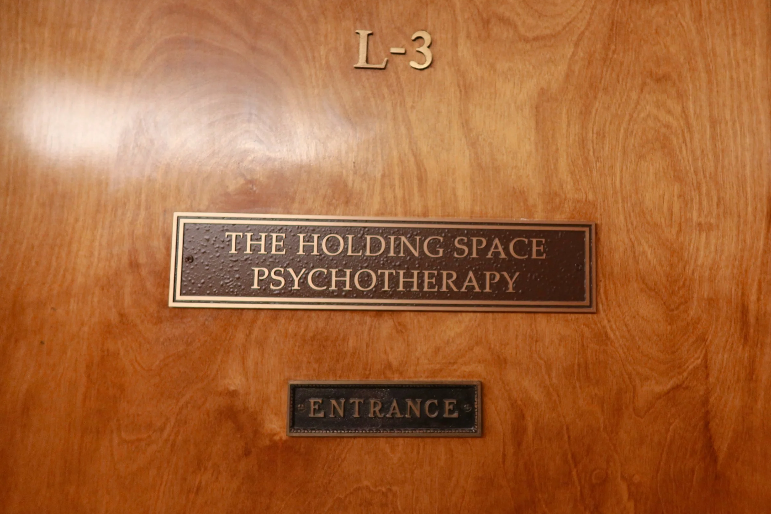 Wooden door with a sign that says "The Holding Space Psychotherapy" and an adjacent smaller sign that says "Entrance."