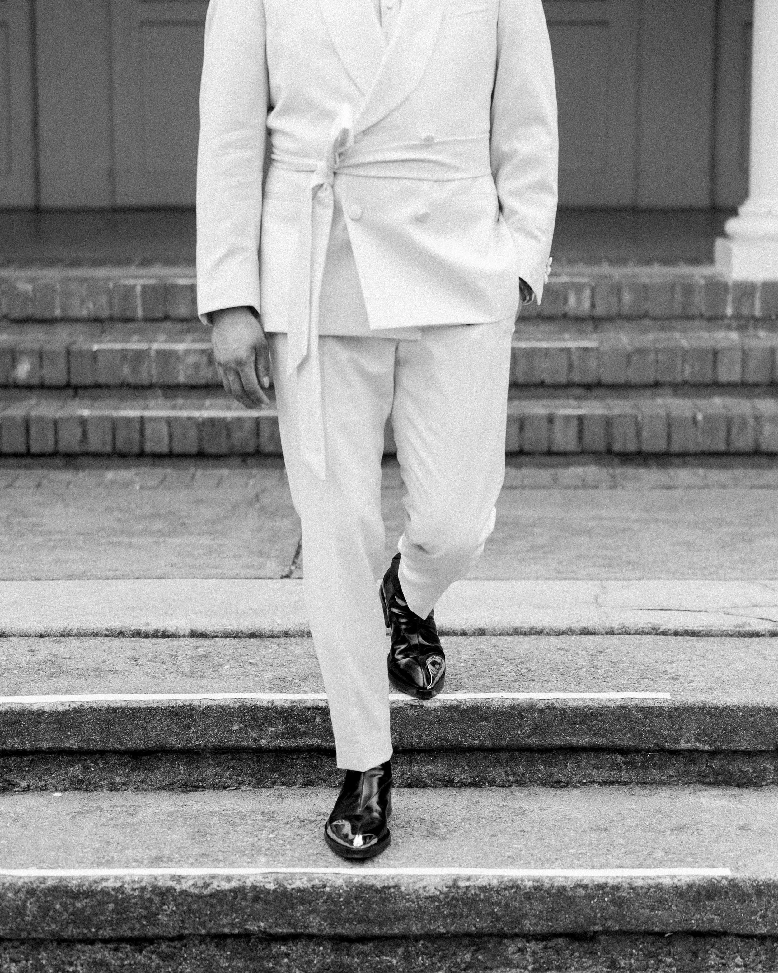 Person in white suit and black shoes walking down steps