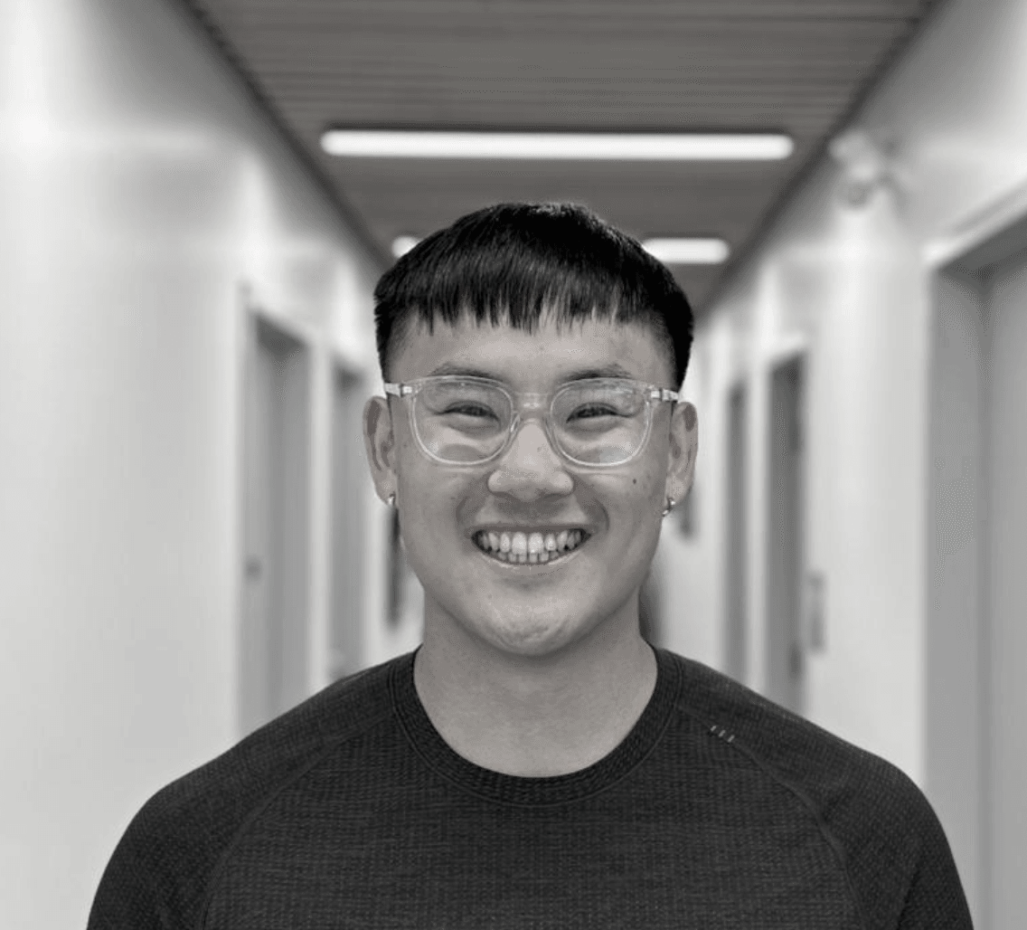 A male Registered Massage Therapist with short dark hair and glasses smiling in a hallway.