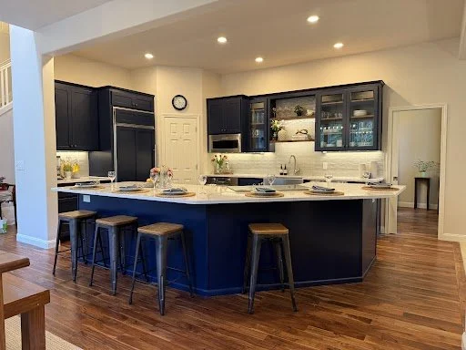 Modern kitchen with navy blue cabinets, a white marble island with seating, and hardwood floors.