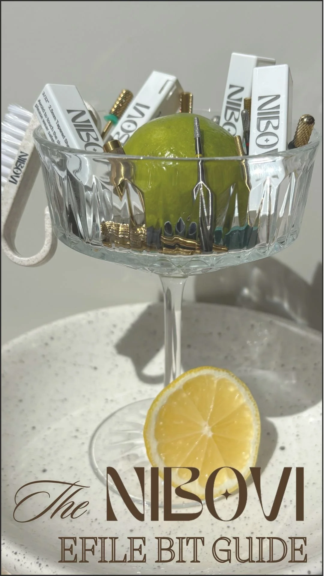 A crystal cocktail glass with a green apple, lemon half, and dental tools inside, placed on a white speckled surface with a white background, with the text "The NIBOVI FILE BIT GUIDE" overlaid.
