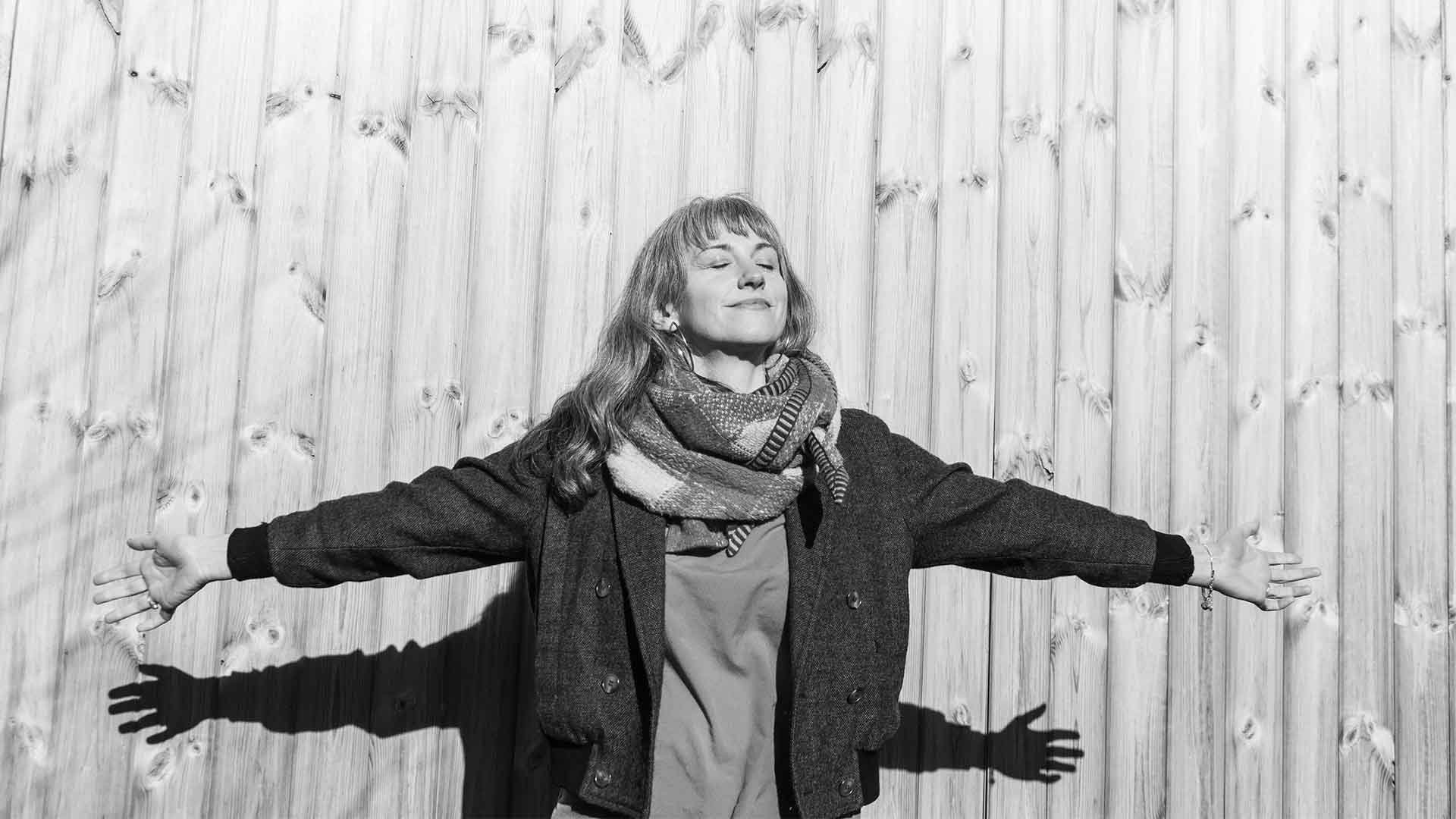 Photo of musician Inni - K standing with arms wide open eyes closed facing towards the sun with a peaceful smile on her face.