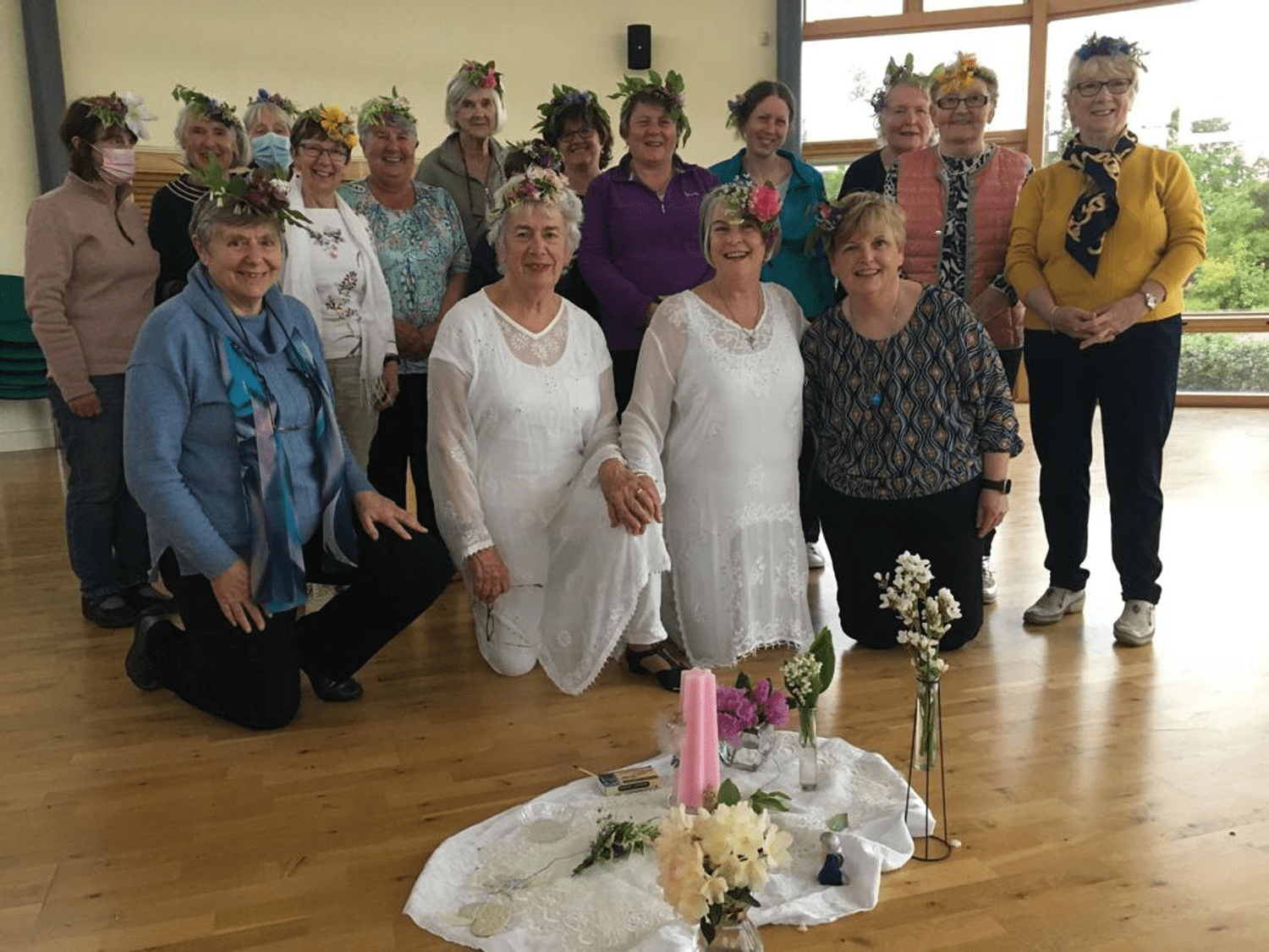 Group from a previous Sacred Circle dance wearing headpieces made with seasonal flowers and greenery, everyone seems delighted to be there.