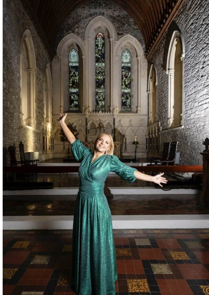 Photo of Celine wearing a green glittery dress with arms out stretched at the alter in St Brigid's Cathedral