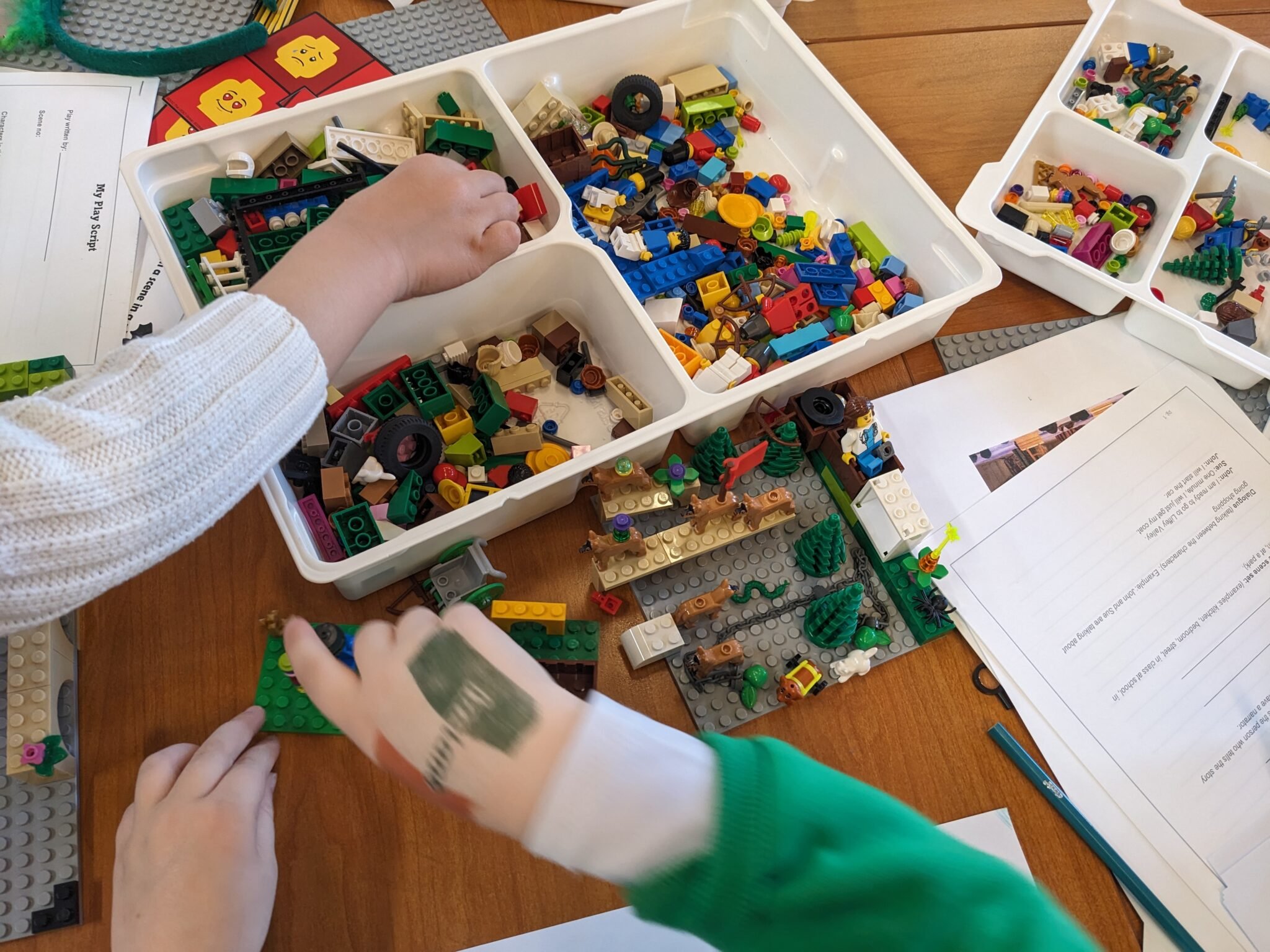 Photo of children playing with lego, lots of clours and types of lego in a white box