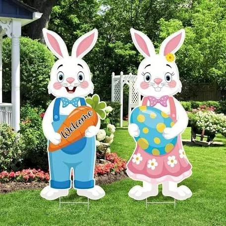 Photo of two friendly bunnies one holds a Welcome sign dressed in blue overalls, the other holds a blue easter egg wearing a pink dress
