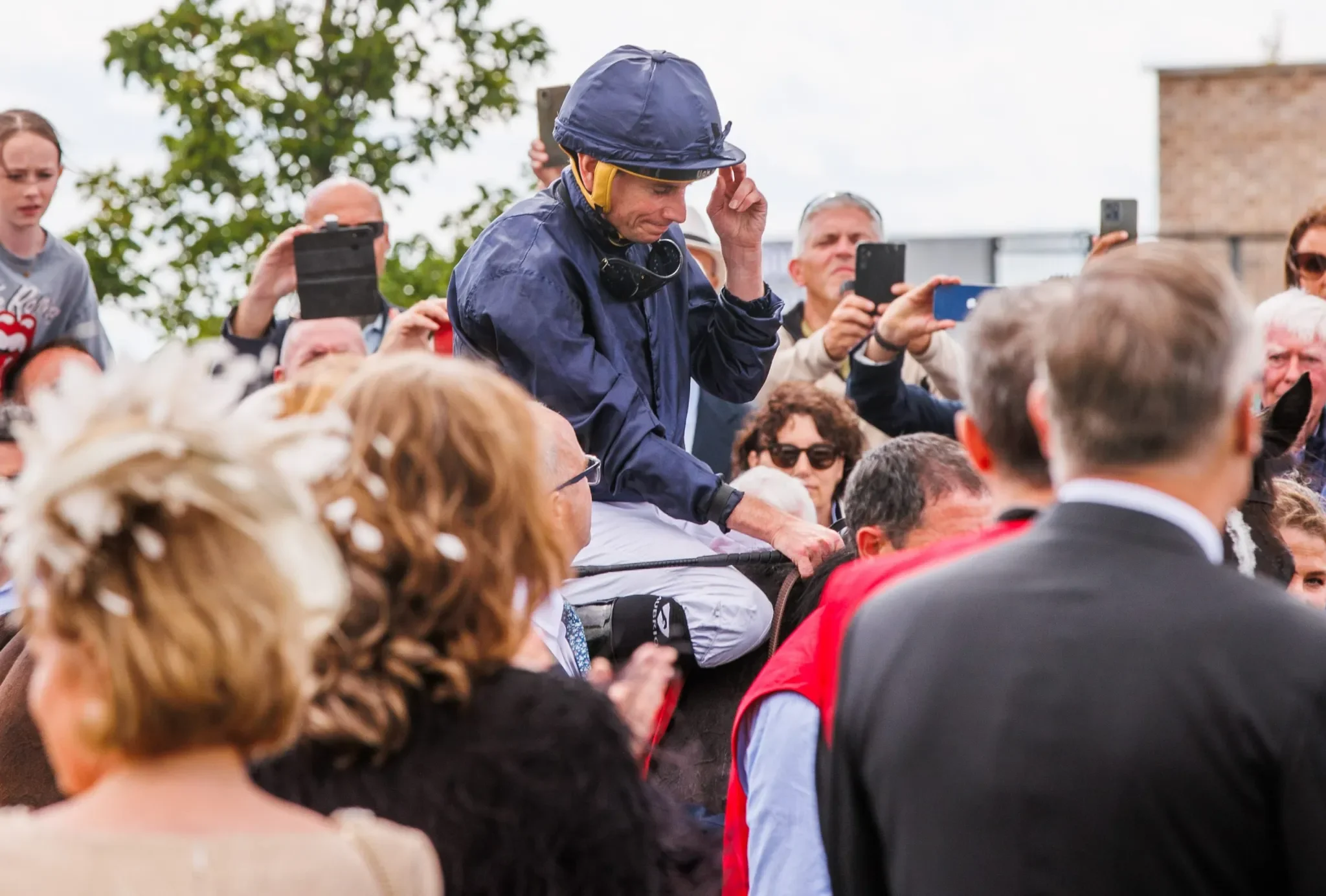 jockey  on racehorse with people round him at race meeting