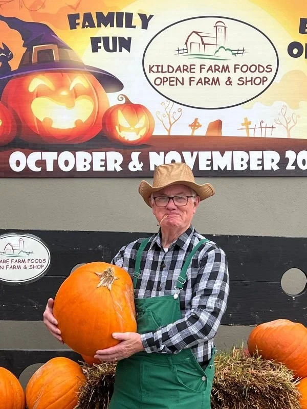 man holding large pumkin with background showing kildare farm foods logo