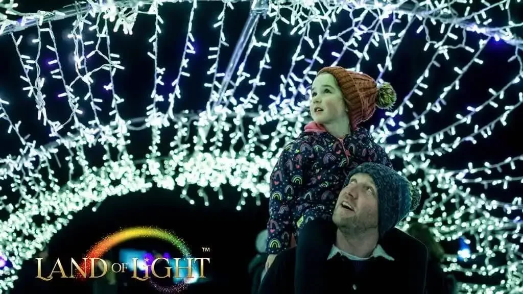 Man with young girl on his shoulders and strings of light in background