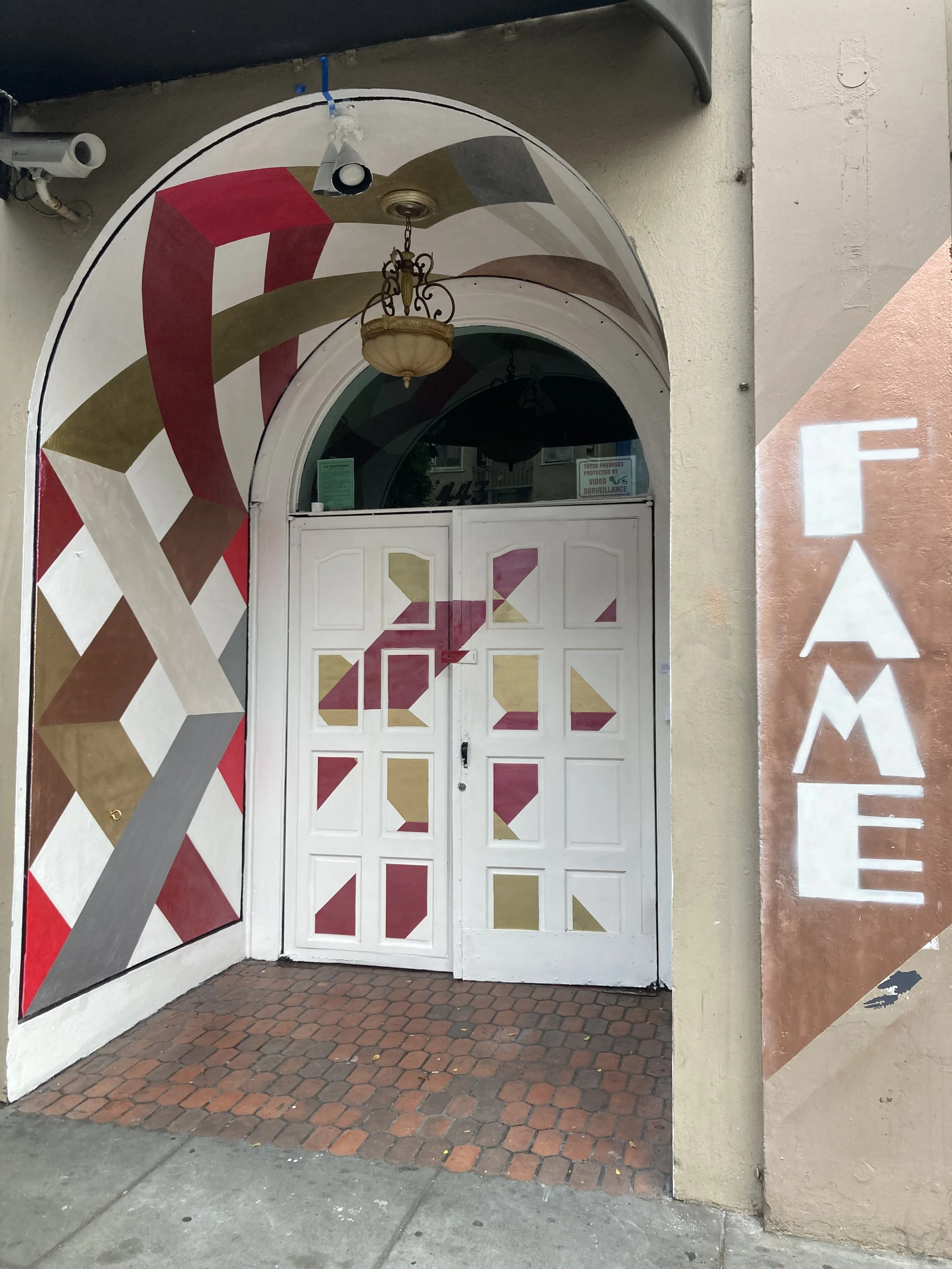 Entrance to a restaurant with painted geometric patterns on the door and archway, and a vertical sign reading 'FAME' on the right side.