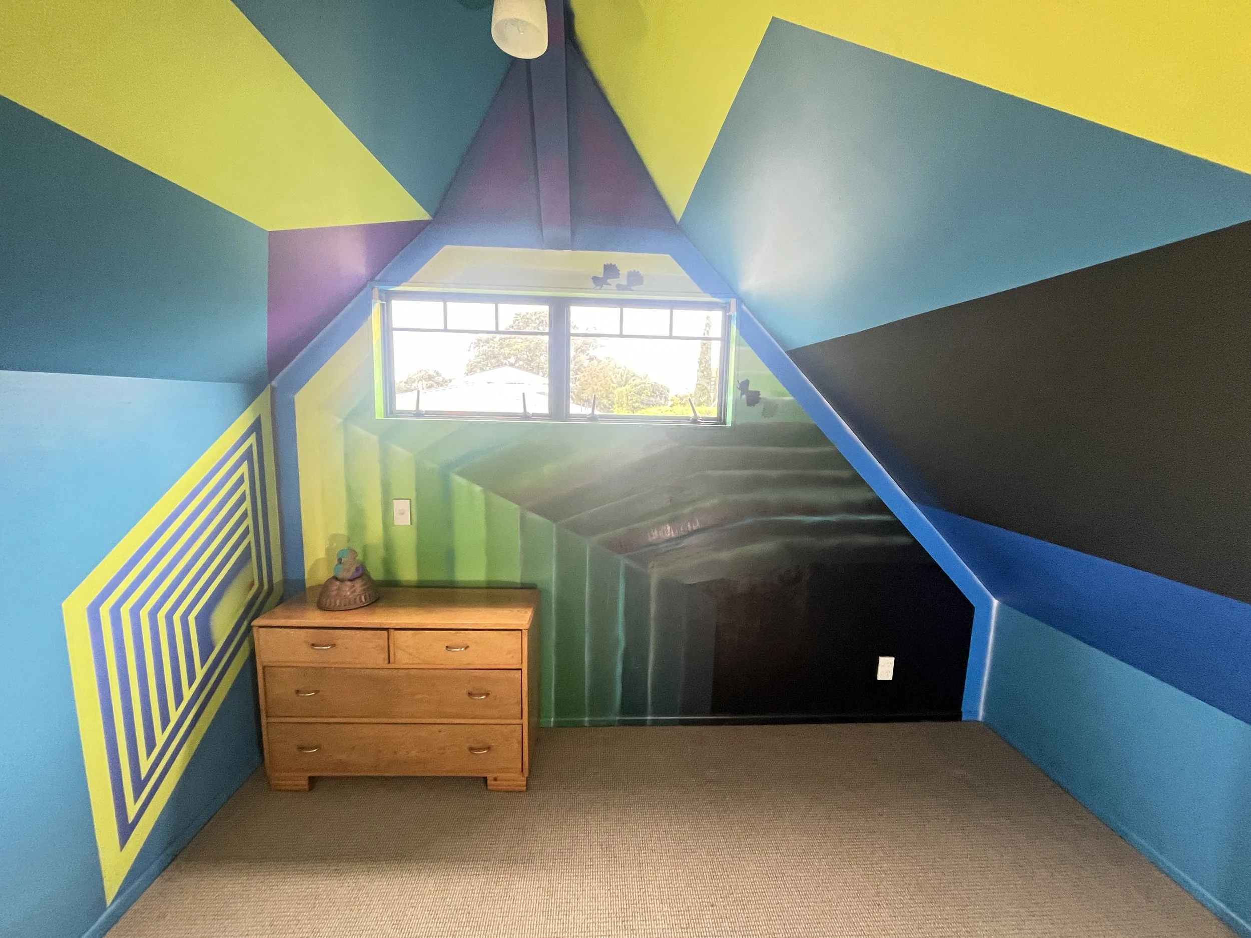 Colorful attic room with geometric painted walls, a small wooden dresser, and a window allowing natural light.