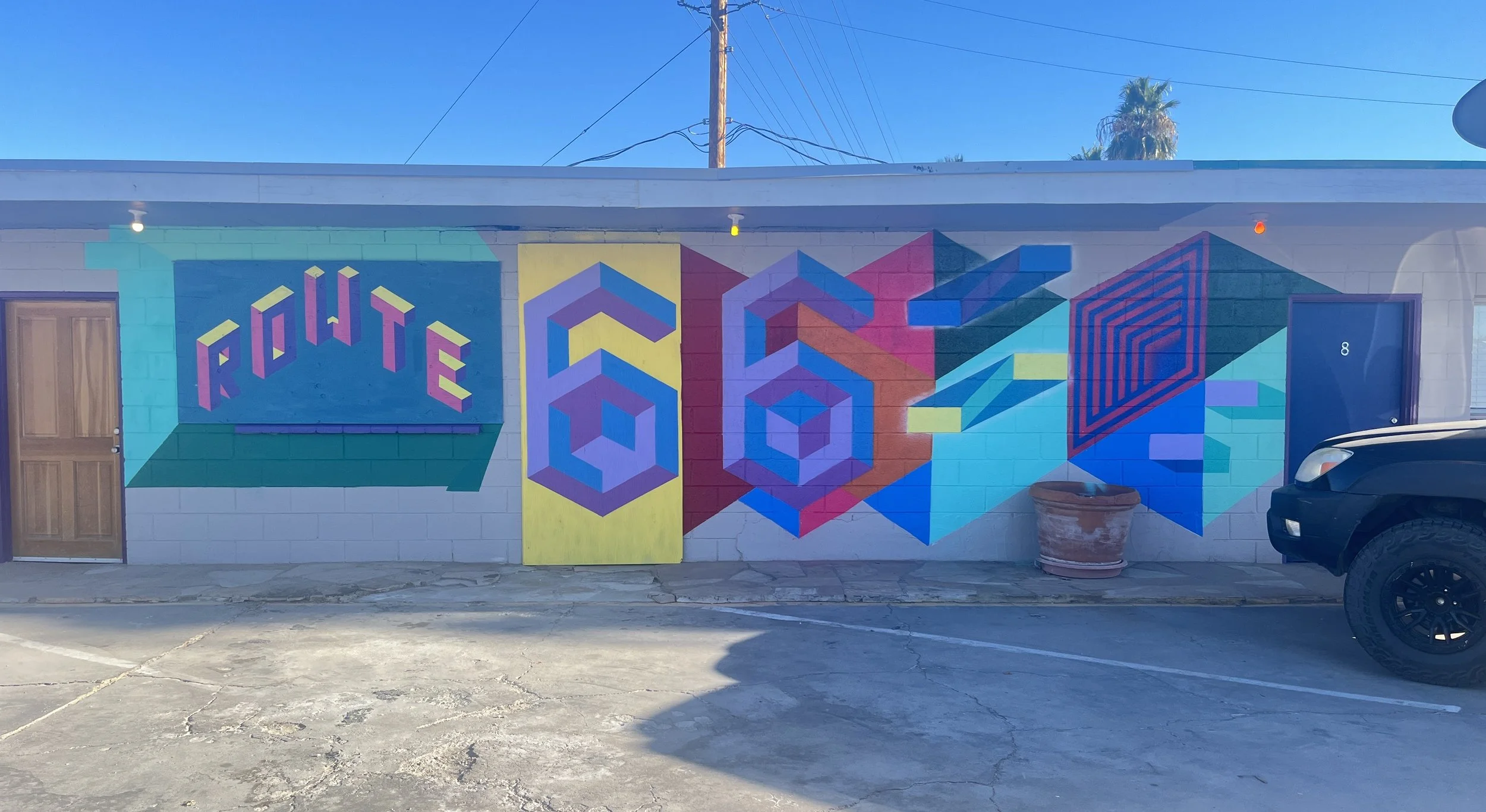 Colorful mural on a white brick wall with the word 'ROUTE' in pink, purple, and yellow geometric shapes and patterns.