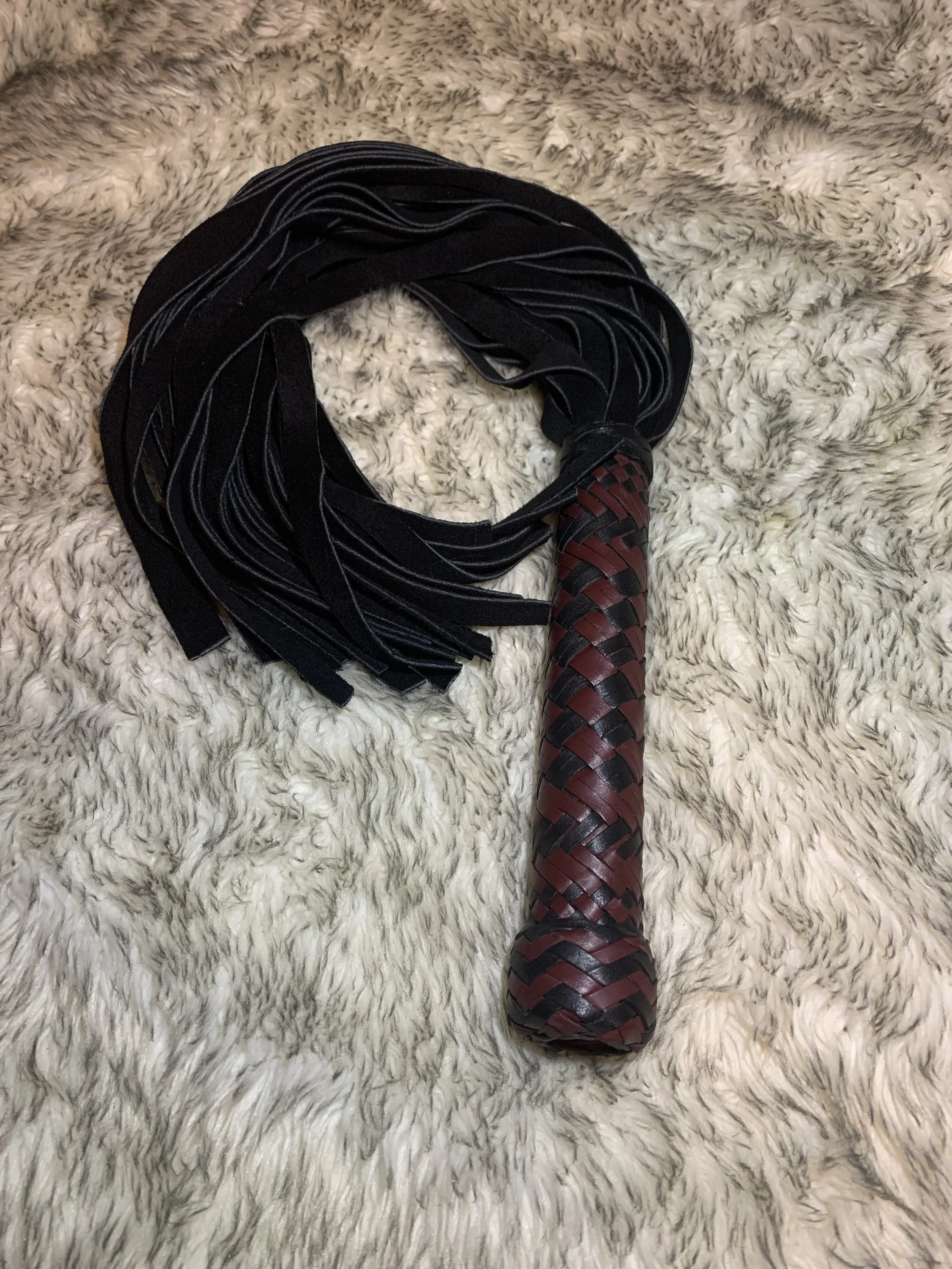 A suede flogger with a handle wrapped in red and black braided kangaroo leather.