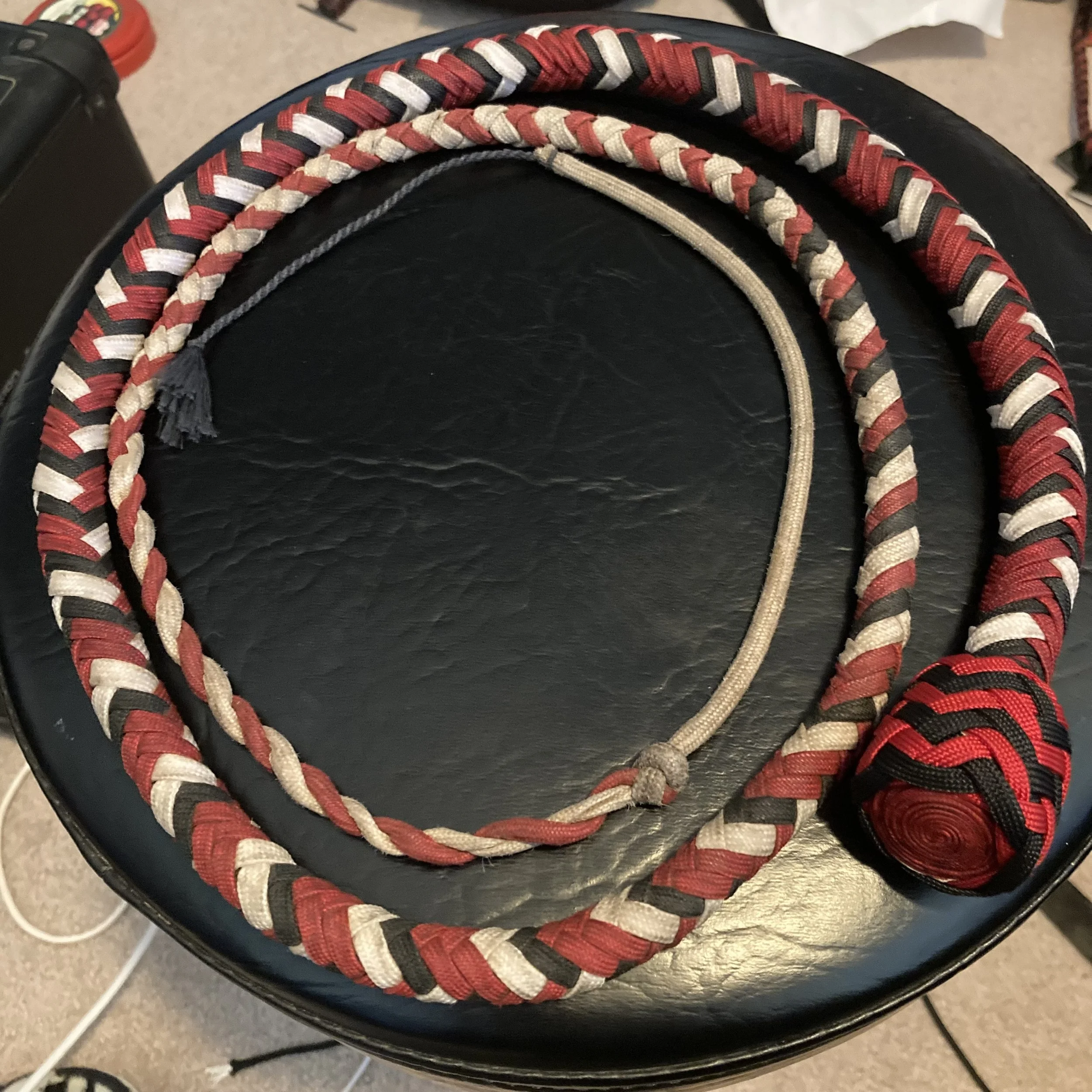 Three braided ropes, two with red, black, and beige colors, and one beige, coiled on a black surface.