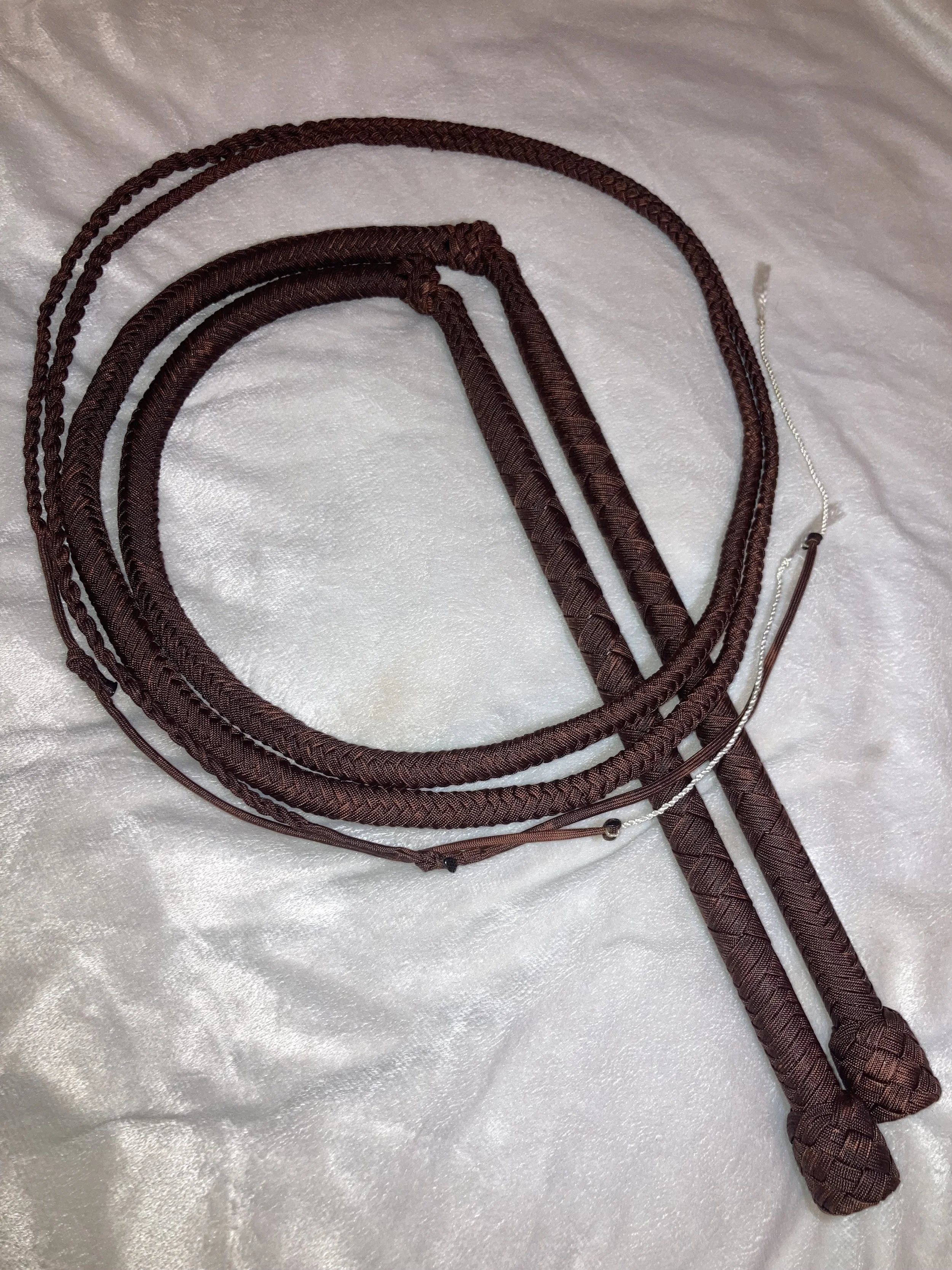 Three brown braided whip lanyards with metal clips and knots, resting on a white satin surface.