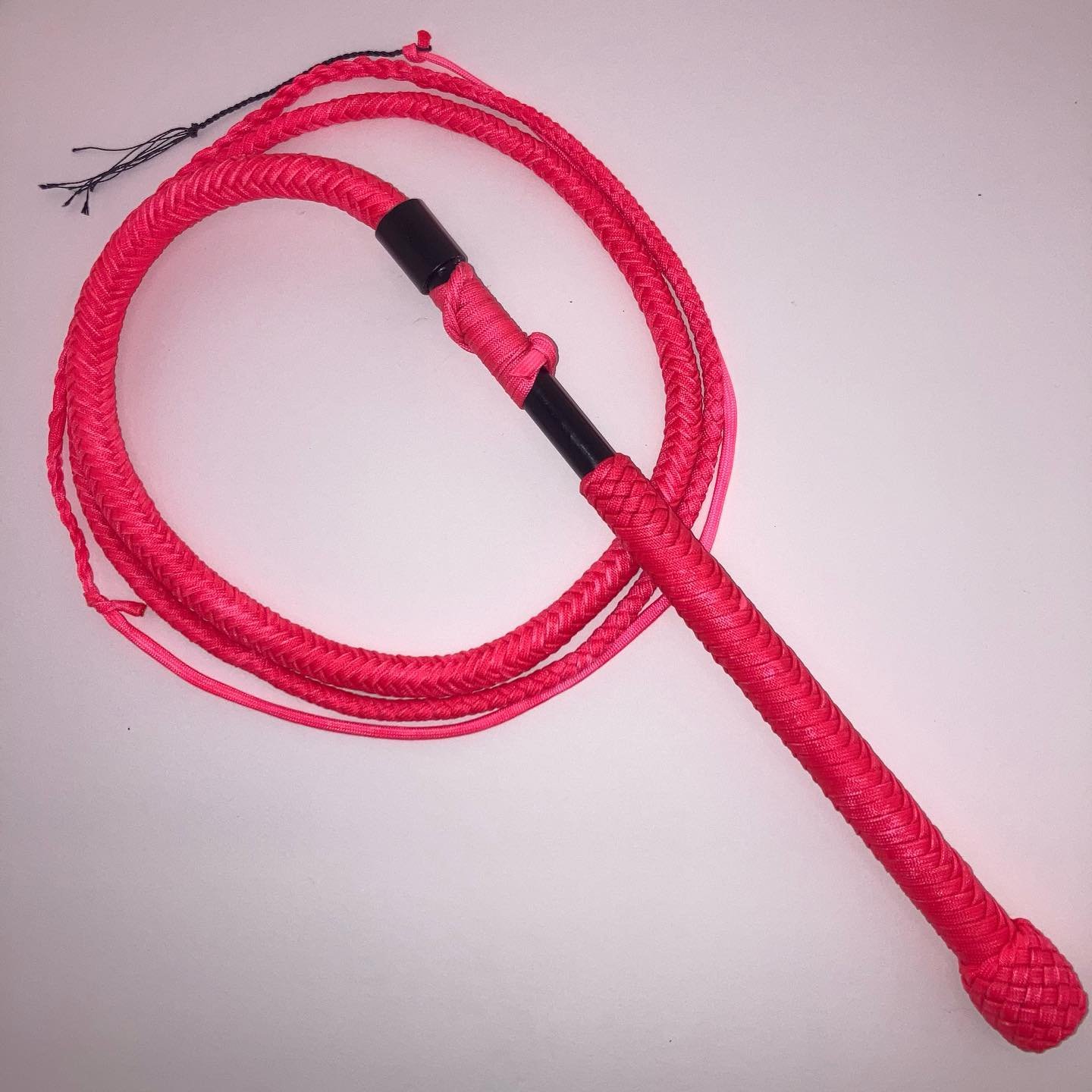 Pink jump rope with black handles on a plain background.