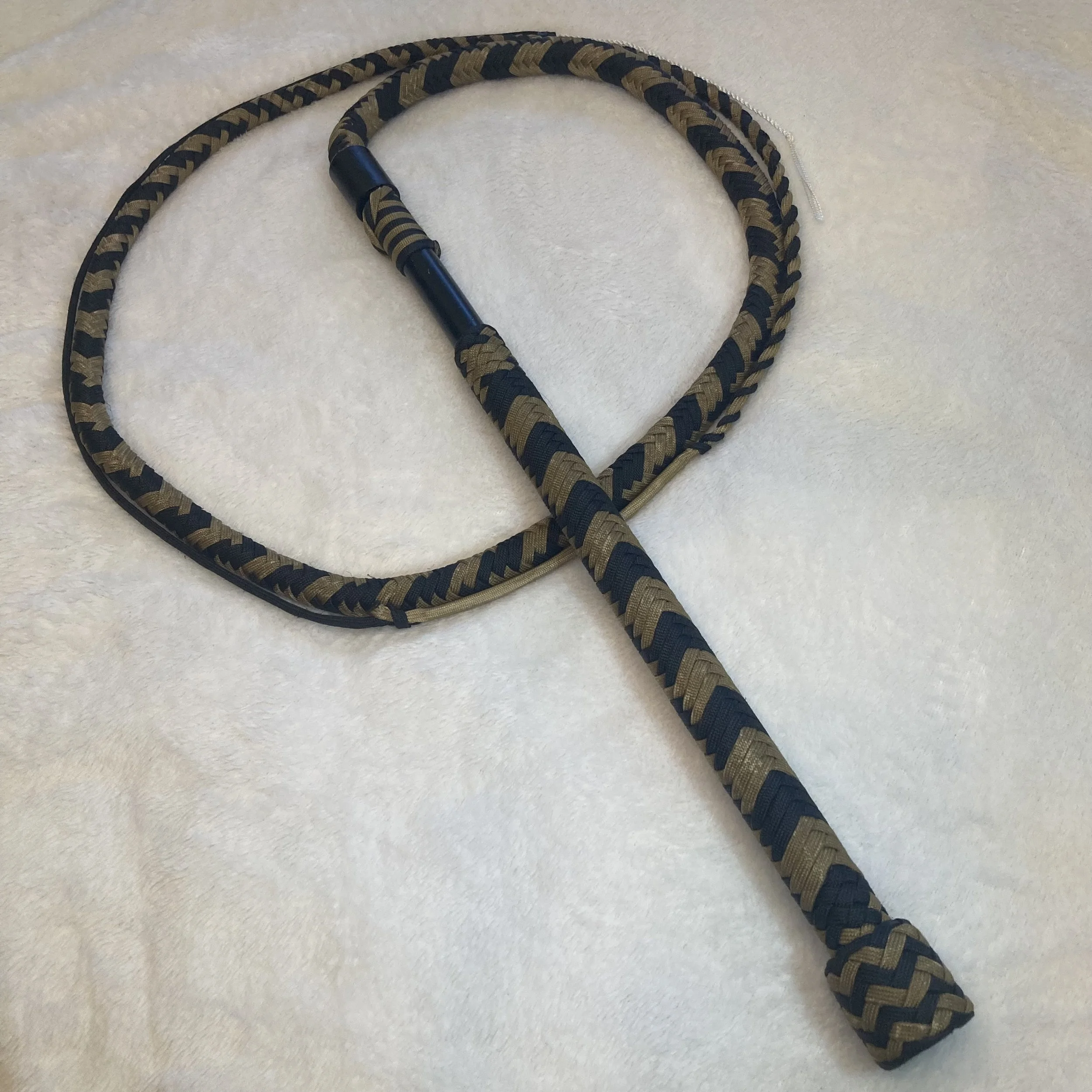 A jump rope with a black and gold braided design, lying on a light-colored textured surface.