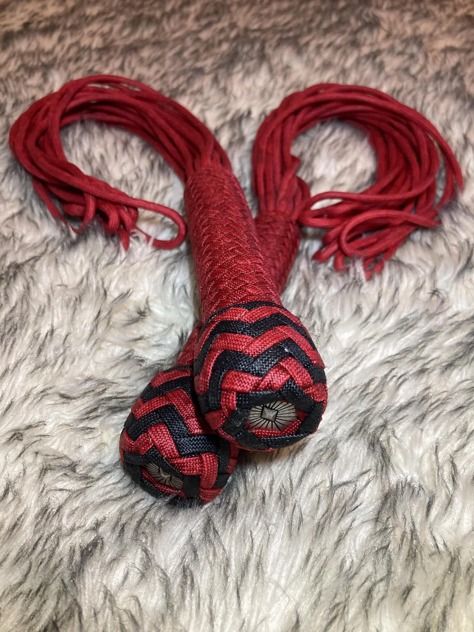 Red and black braided jump rope lying on a fluffy white surface.