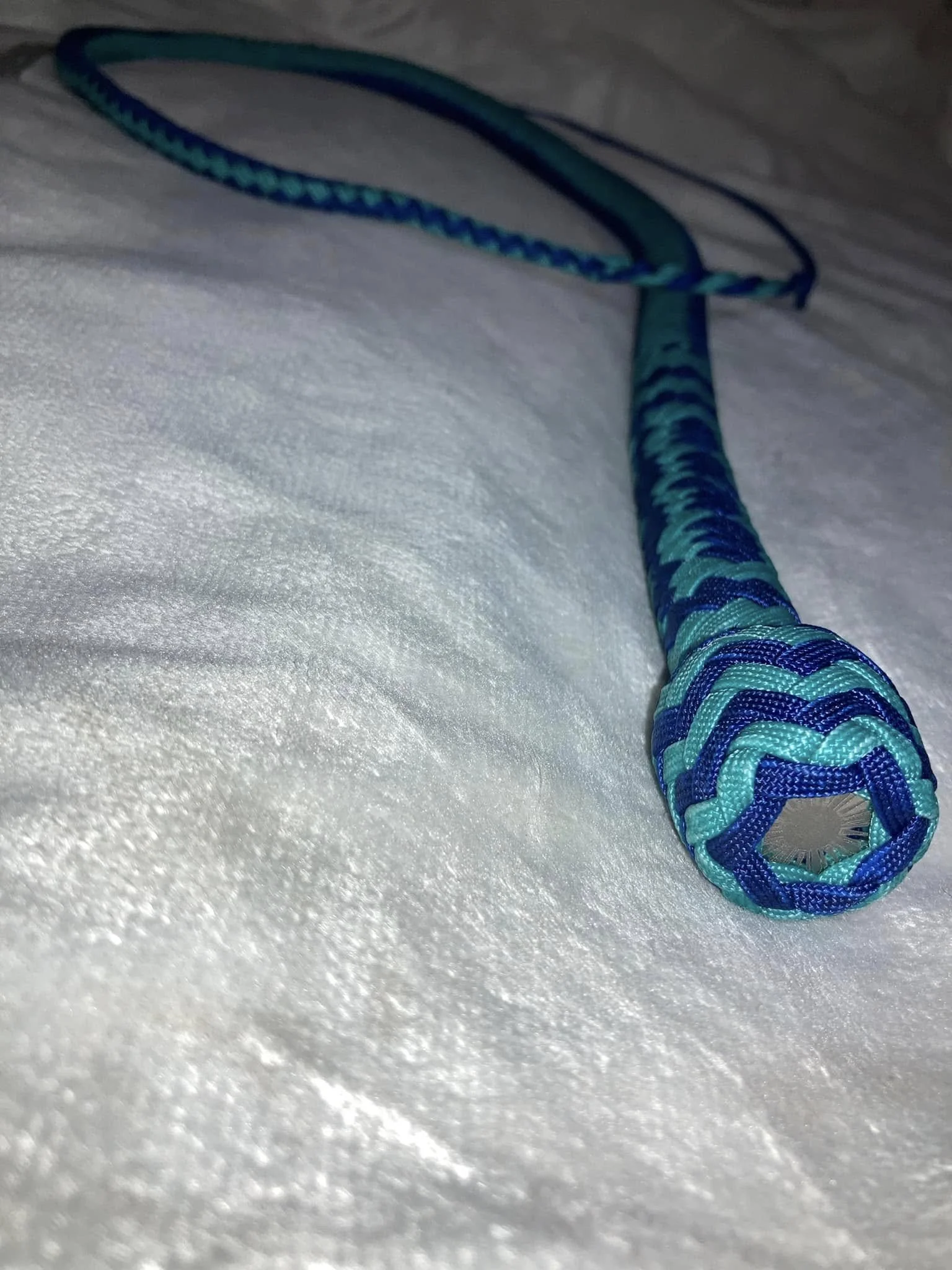 A blue and green braided rope with a loop at one end, resting on a white textured surface.