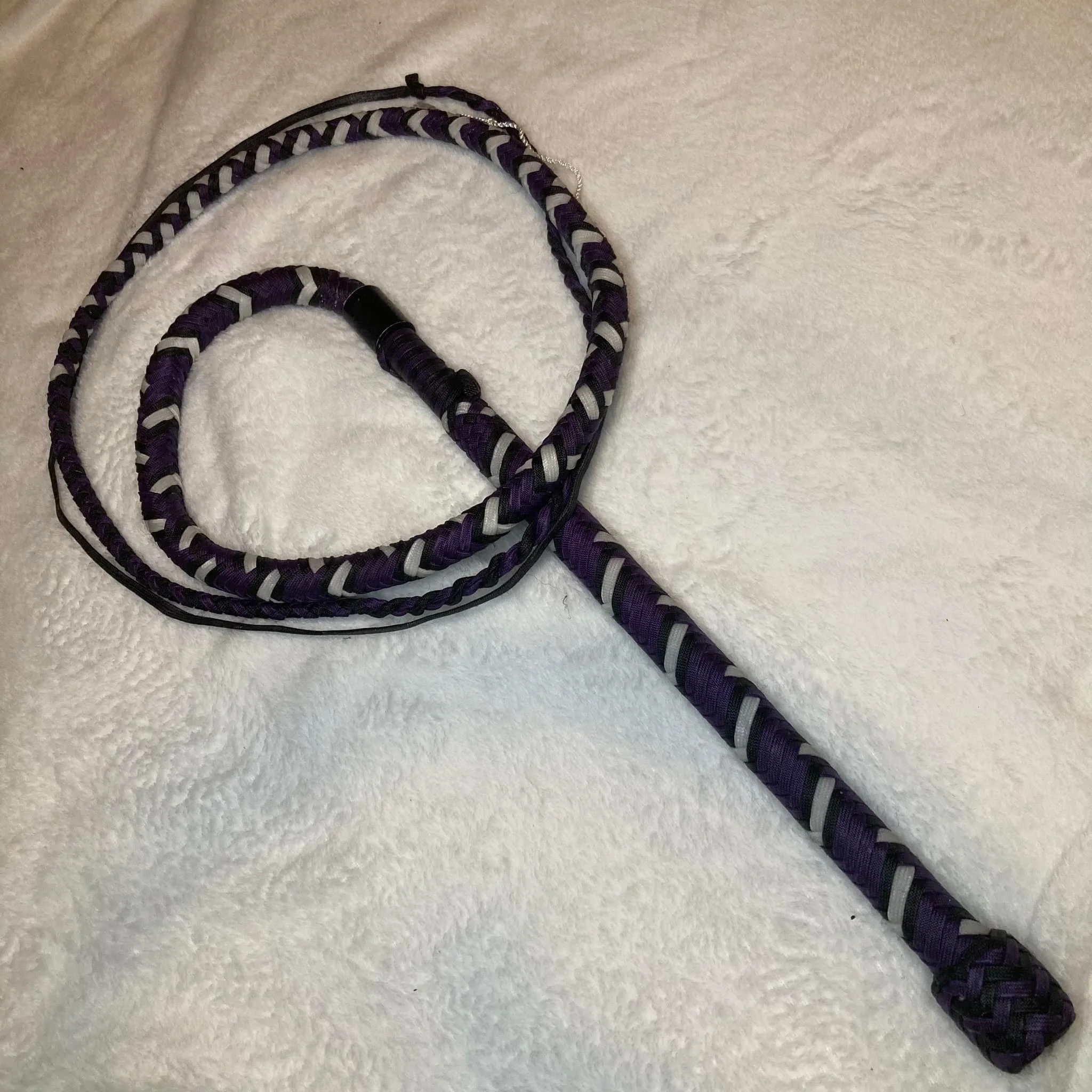 A purple and black braided jump rope with a black handle, resting on a white textured surface.