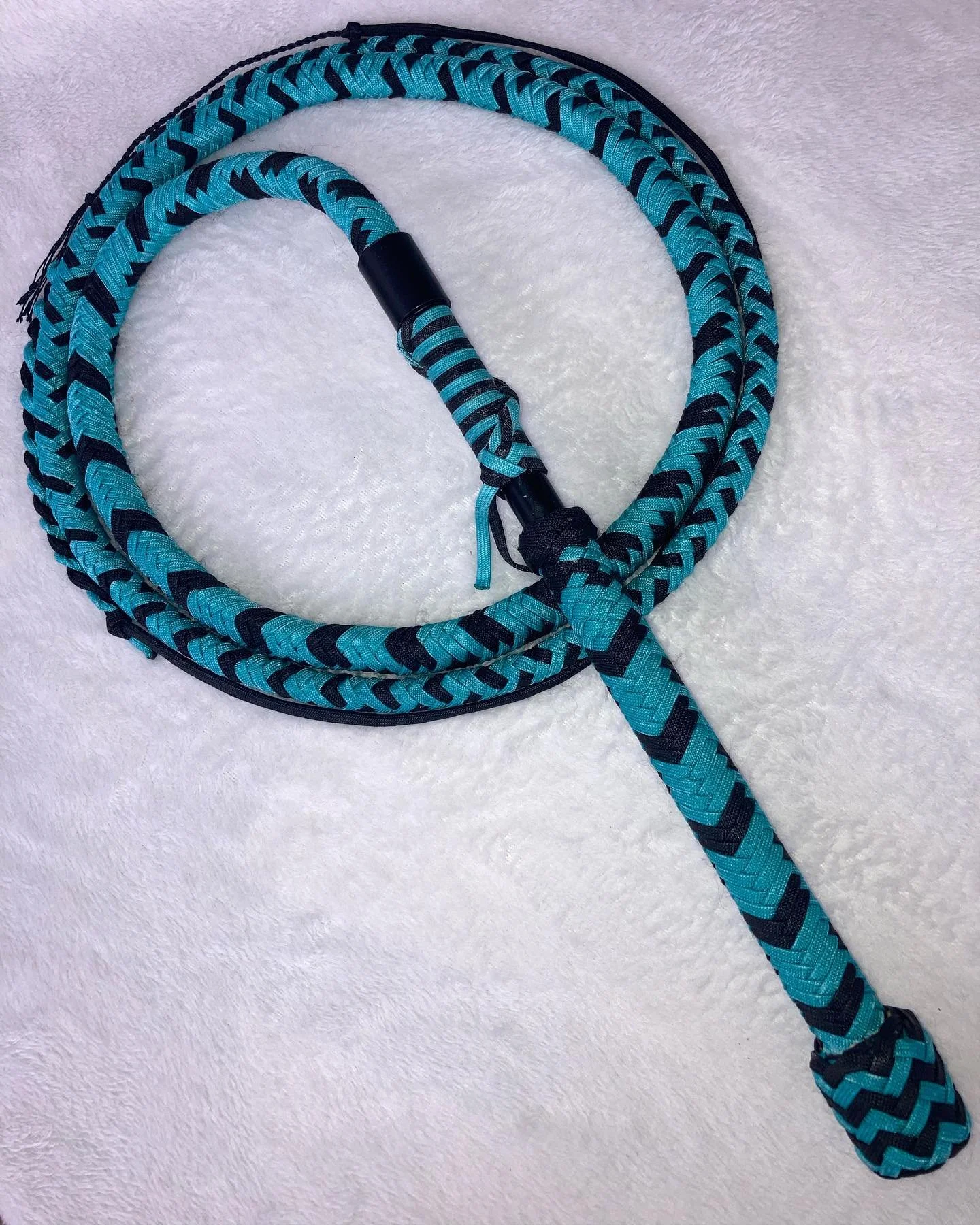 A blue and black woven jump rope with handles, resting on a white fluffy surface.
