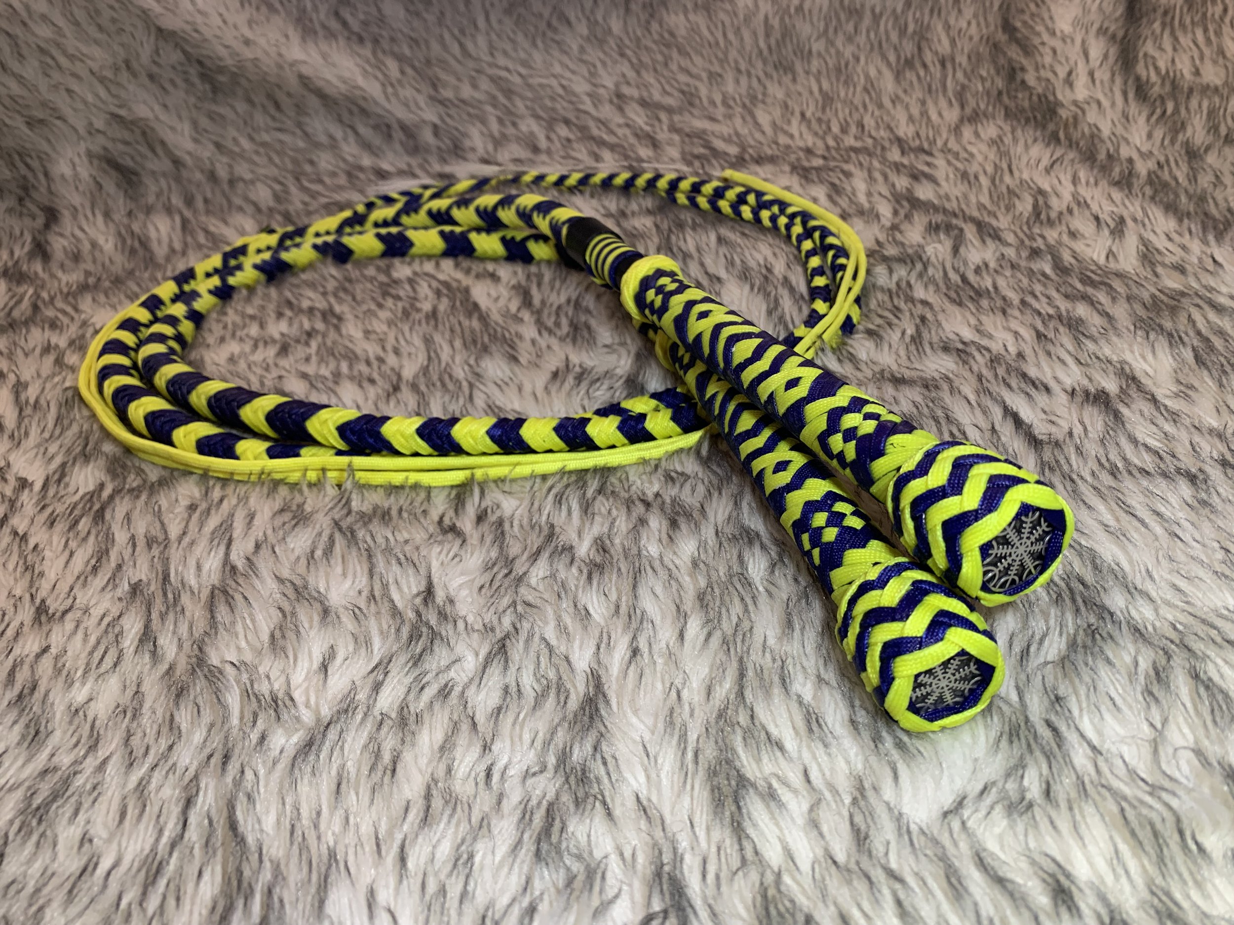 Yellow and purple braided jump rope with snowflake symbols on the handles, resting on a soft, gray, furry surface.