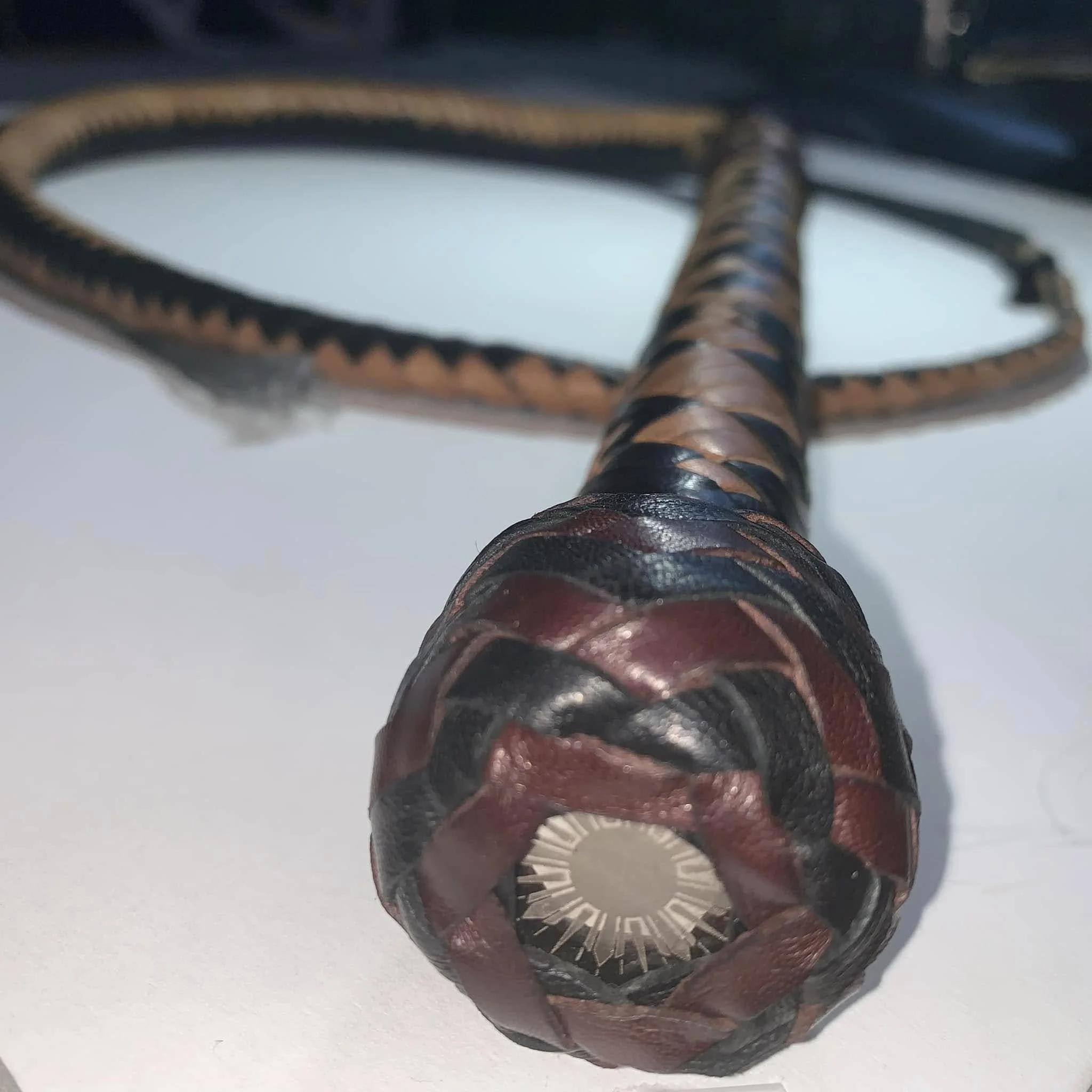 Close-up of a handcrafted kangaroo leather bullwhip with a Turk's Head knot holding a custom laser-engraved coin.