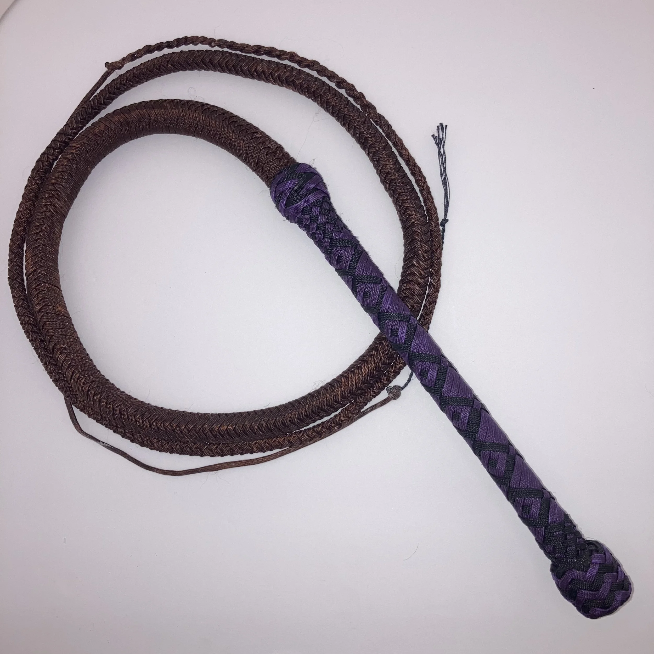 A braided purple and black whip resting on a white surface.