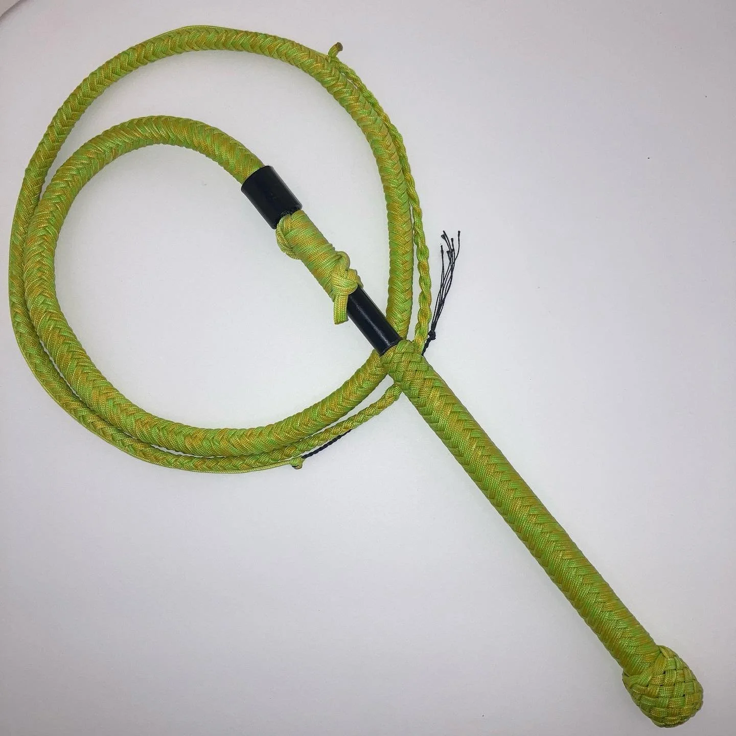A green woven lasso with a black handle and frayed ends, laid flat on a white surface.